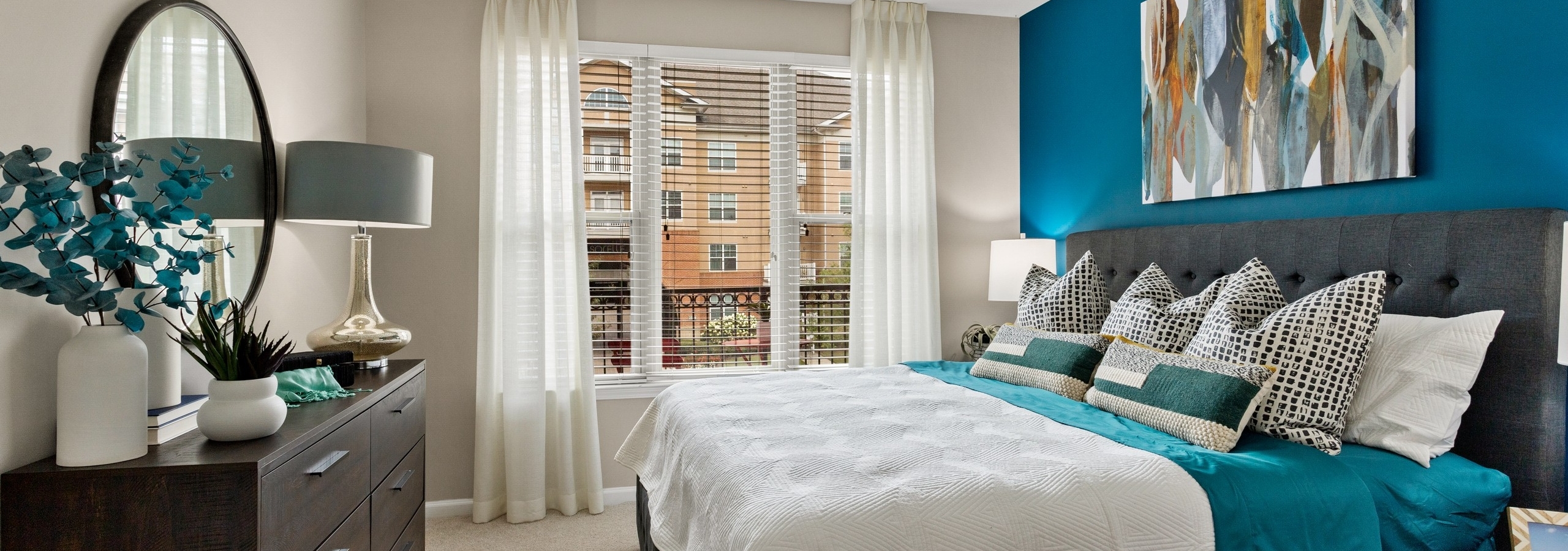 Bedroom at AMLI Lindbergh apartments with king bed on blue wall and dark wood dresser and white curtains over large window