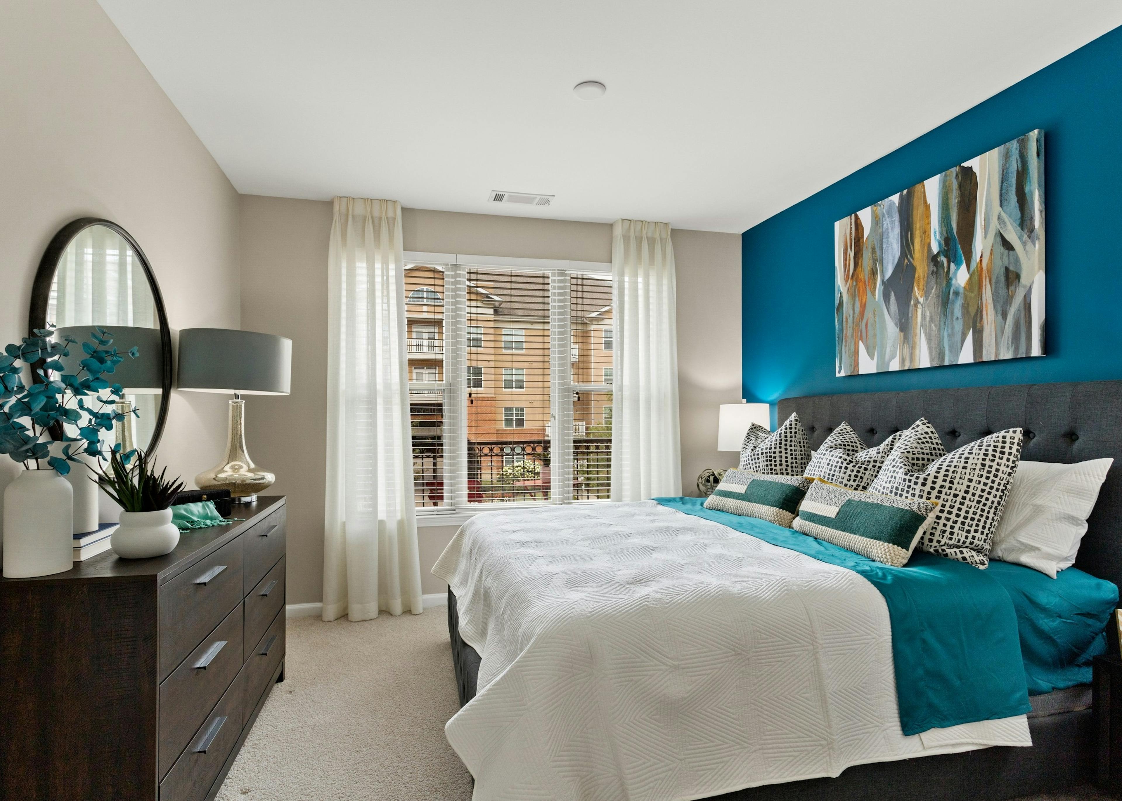 Bedroom at AMLI Lindbergh apartments with king bed on blue wall and dark wood dresser and white curtains over large window