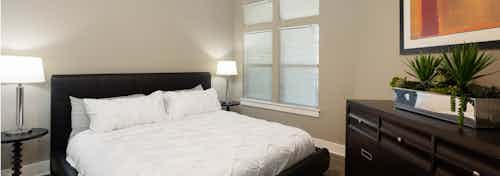 Close up of AMLI 5350 bedroom with black bed frame and white bedding near a tall window with modern lamps on either side