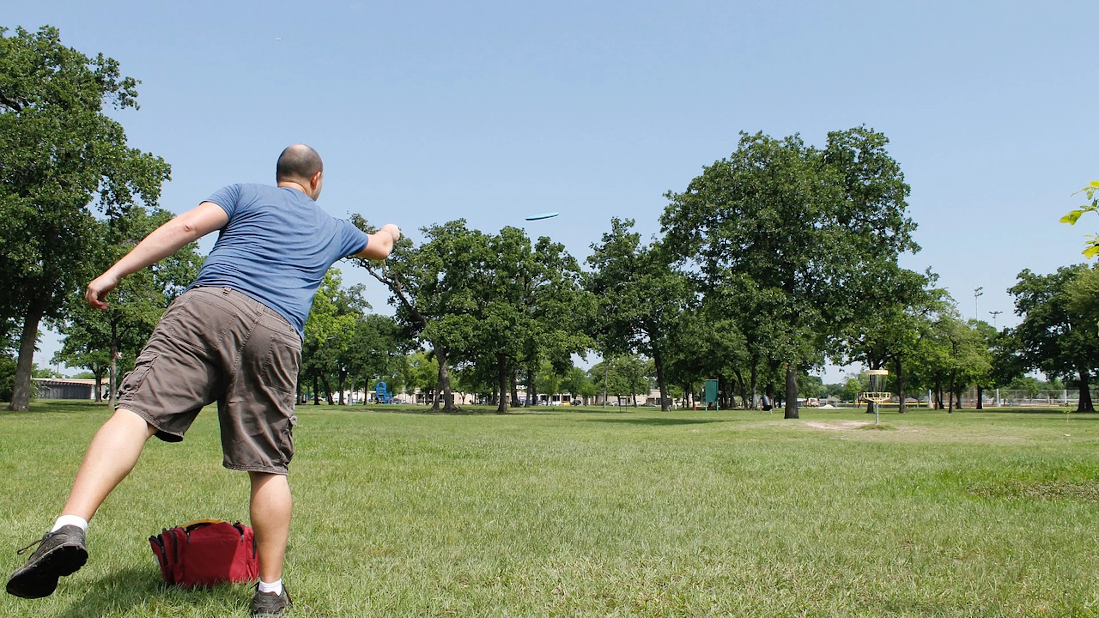 A man in shorts and a tee shirt throwing a Frisbee away from the camera in a large grassy field