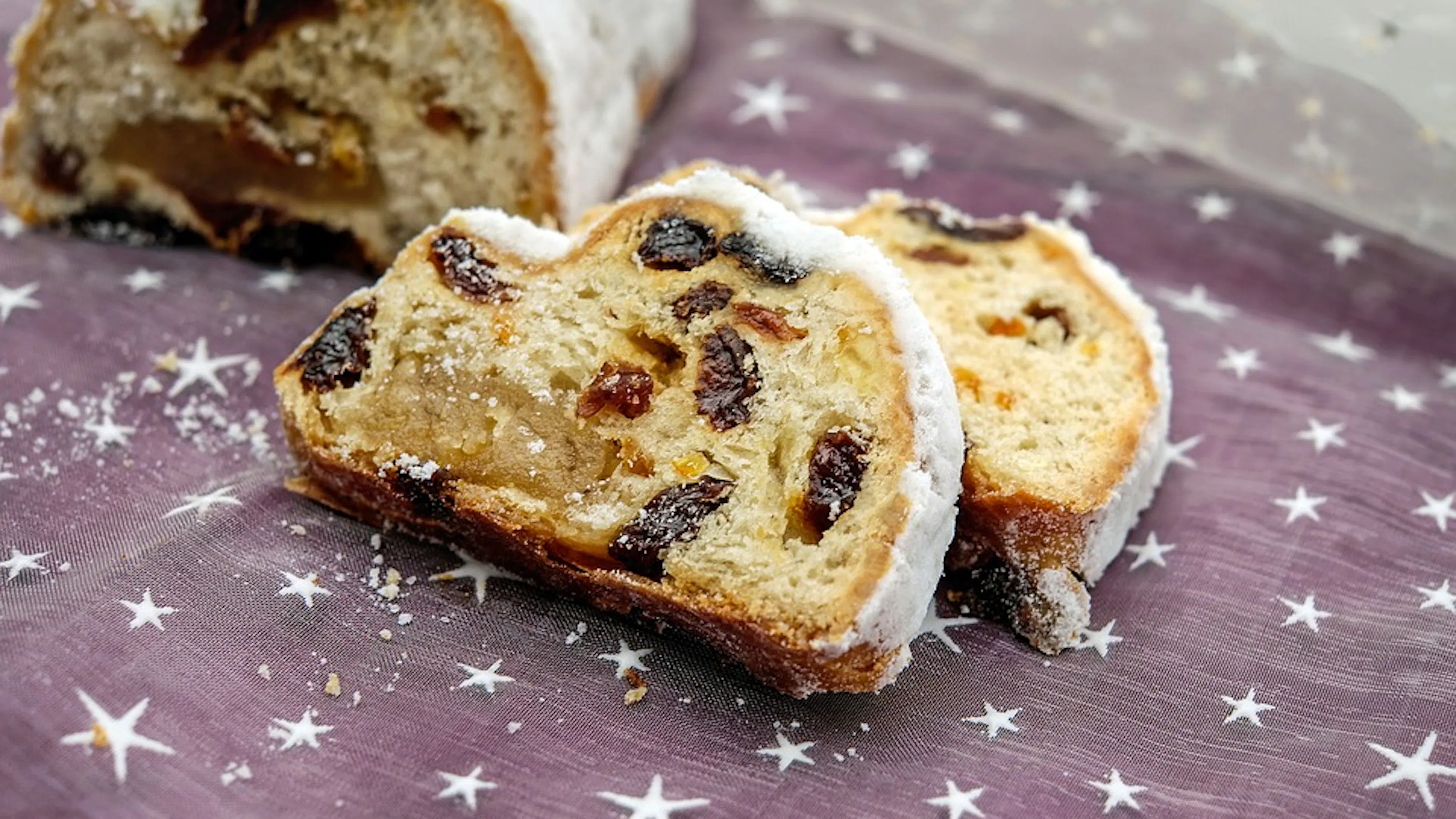 Two slices of stollen Christmas Cake on a light purple tablecloth decorated with small white stars