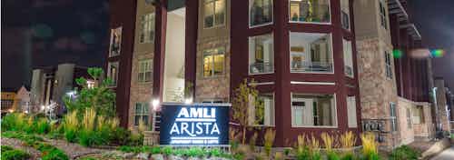 Night time exterior of AMLI Arista apartment building with balconies and several trees and sidewalks and brightly lit signage