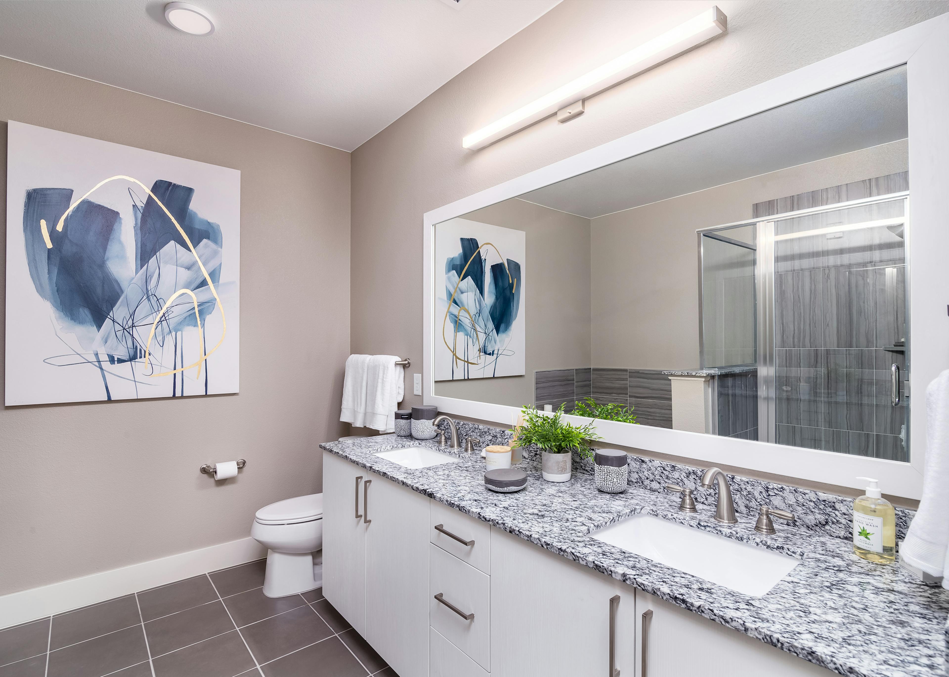 A bathroom at AMLI Littleton Village apartments with a granite counter and two sinks and a large mirror and white cabinets