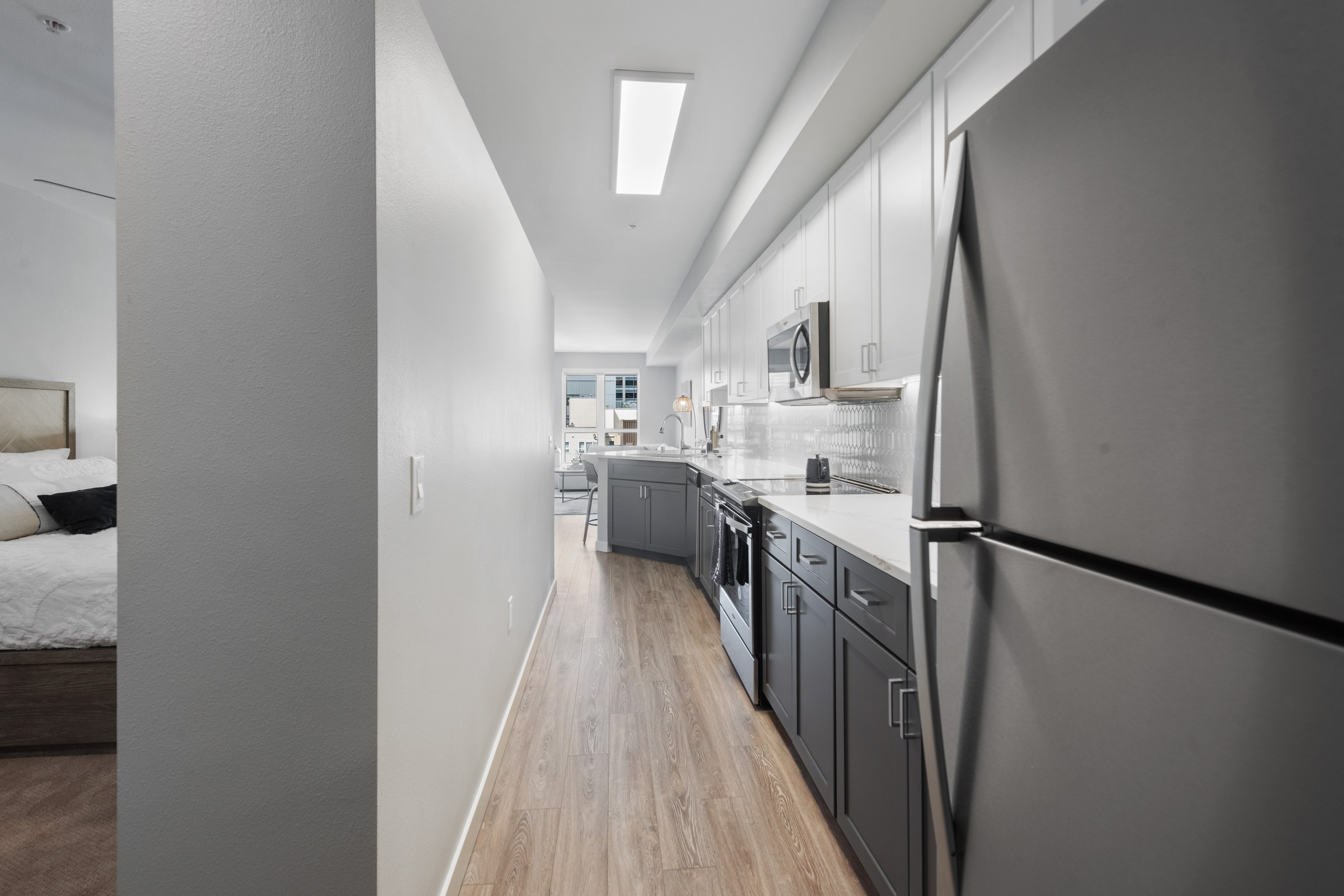 Long view of AMLI 535 apartment kitchen with grey lower cabinets and white upper cabinets with refrigerator and plank flooring