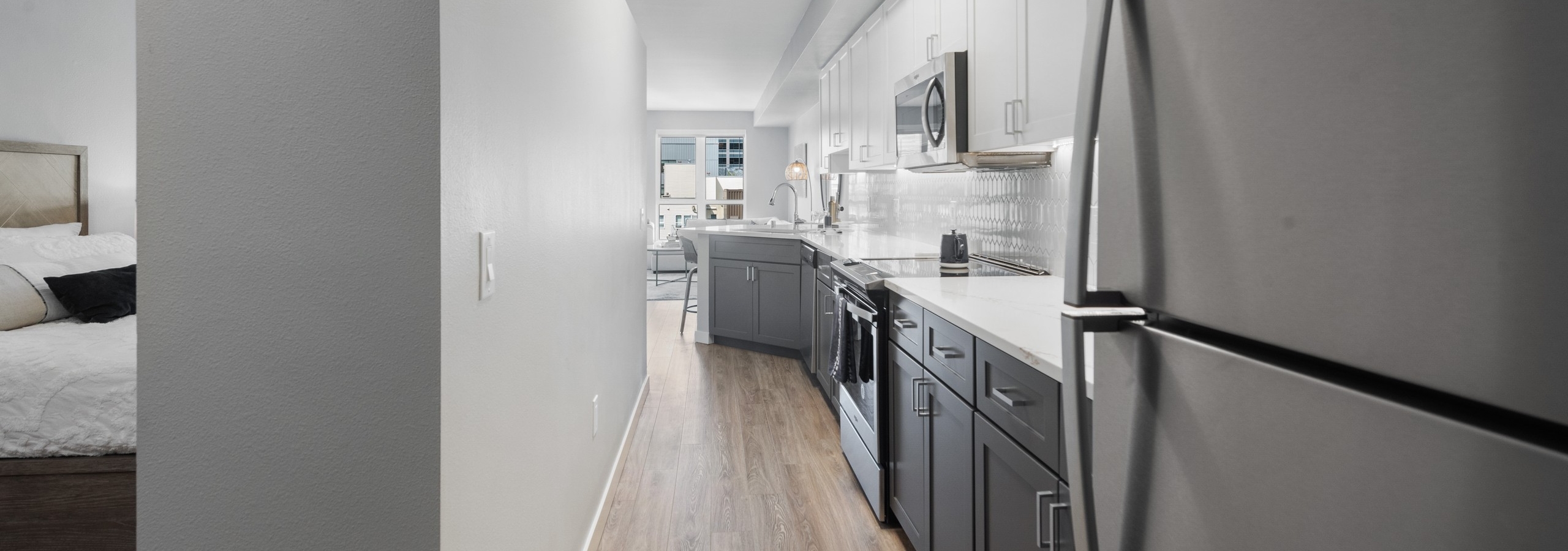 Long view of AMLI 535 apartment kitchen with grey lower cabinets and white upper cabinets with refrigerator and plank flooring