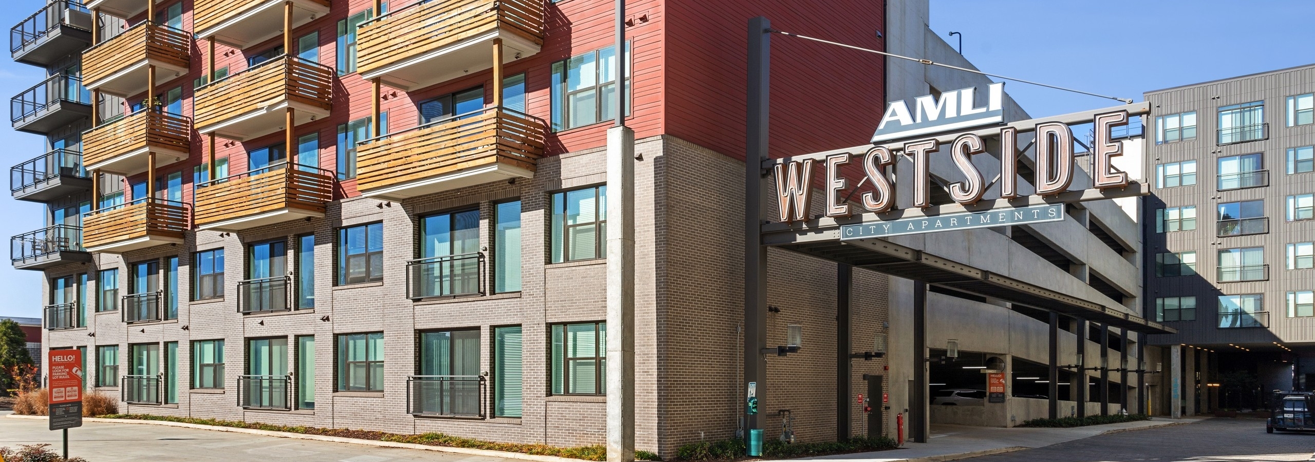 Exterior daytime view of AMLI Westside apartment brick façade with wooden rustic balconies and entrance to parking garage
