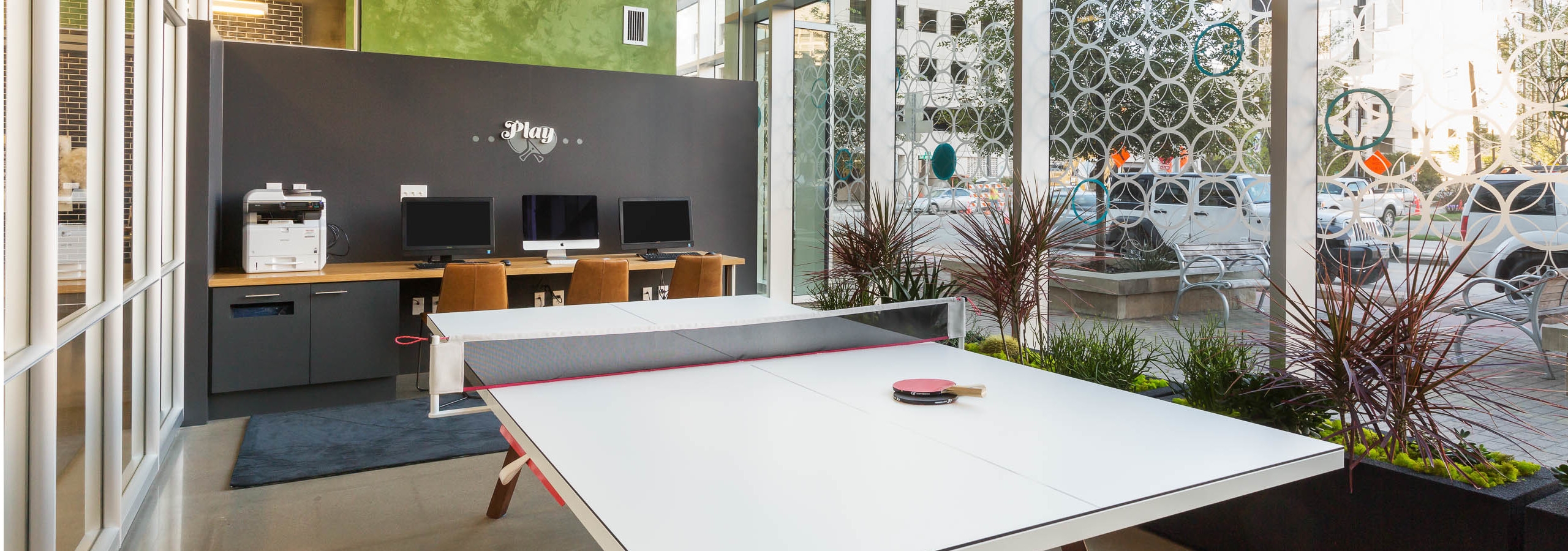 Business center at AMLI on 2nd with a long white table and wooden desk area with three computers and a printer in background