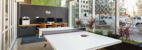 Business center at AMLI on 2nd with a long white table and wooden desk area with three computers and a printer in background