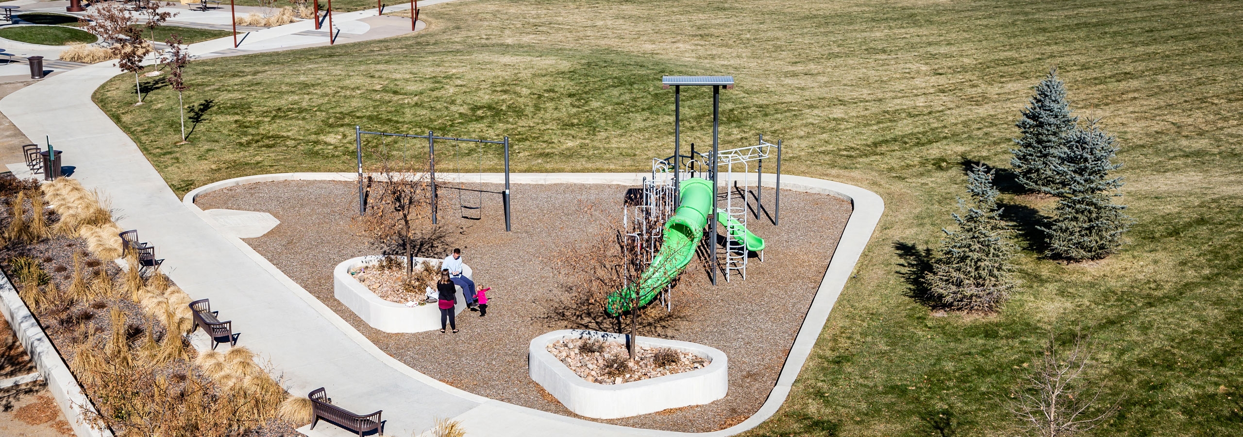 Daytime aerial view of a family at a children’s playground in park adjacent to AMLI Littleton Village apartment building