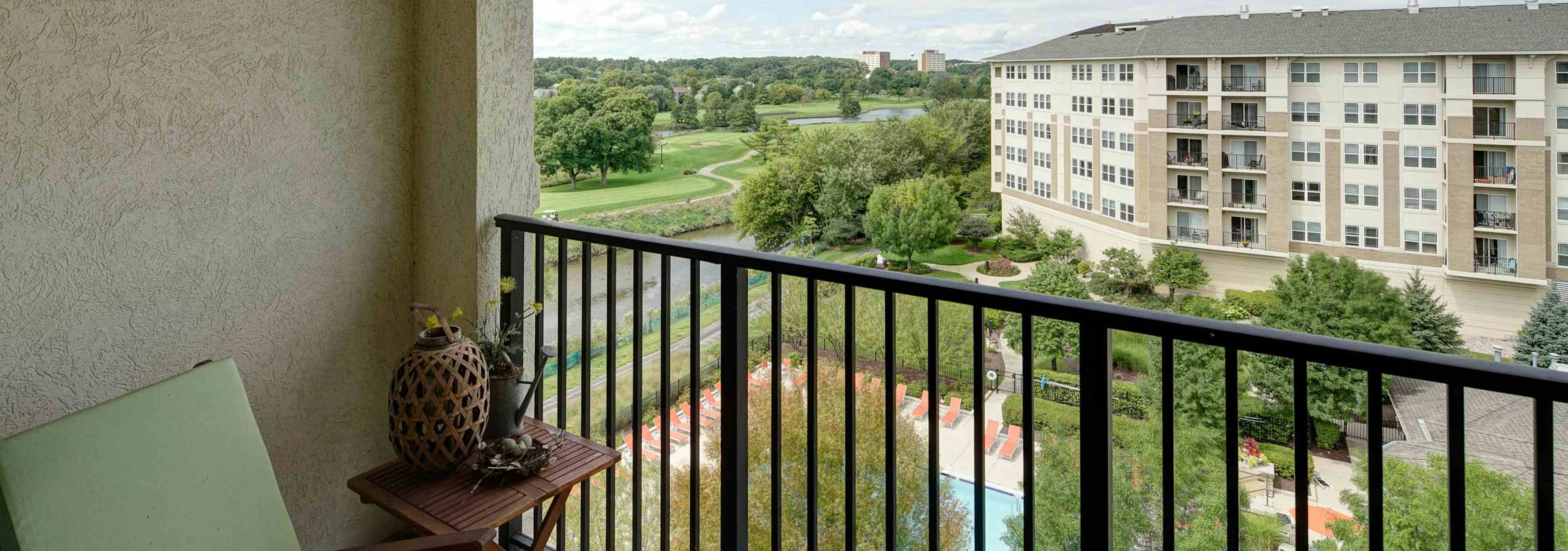 Exterior view from a balcony at AMLI at Seven Bridges overlooking pool area with vibrant green grass and trees