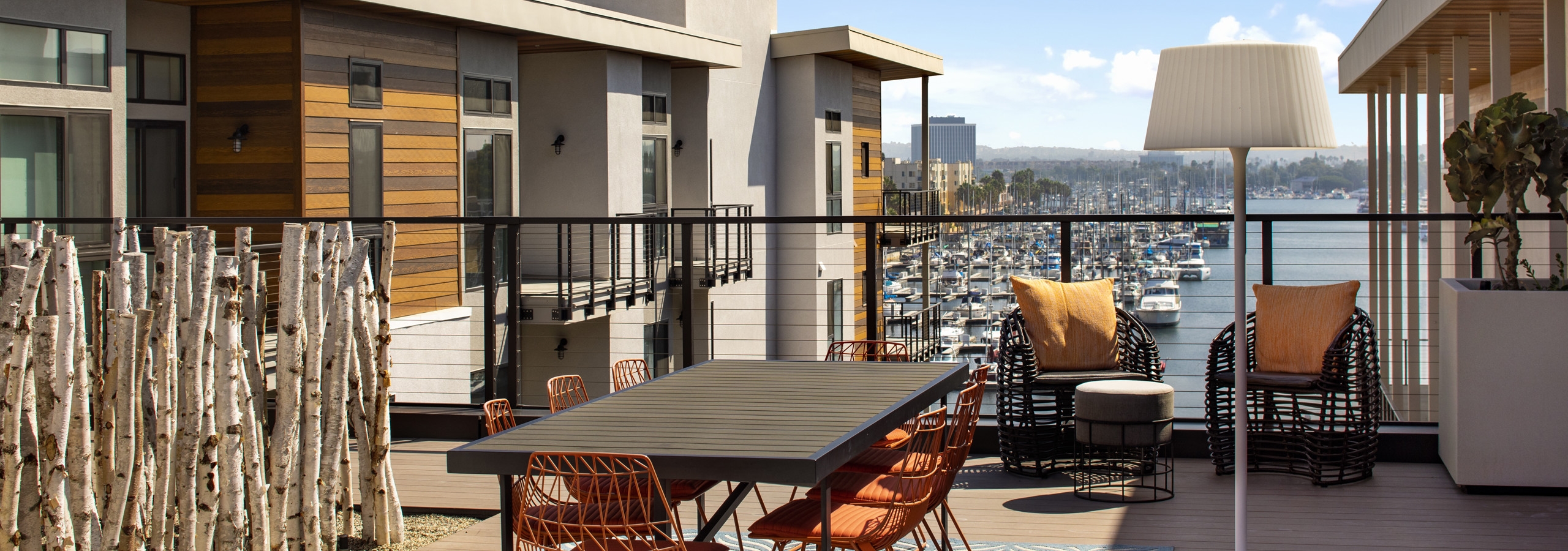 Daytime view of exposed rooftop deck overlooking the marina with a long dining table and orange chairs at AMLI Marina Del Rey