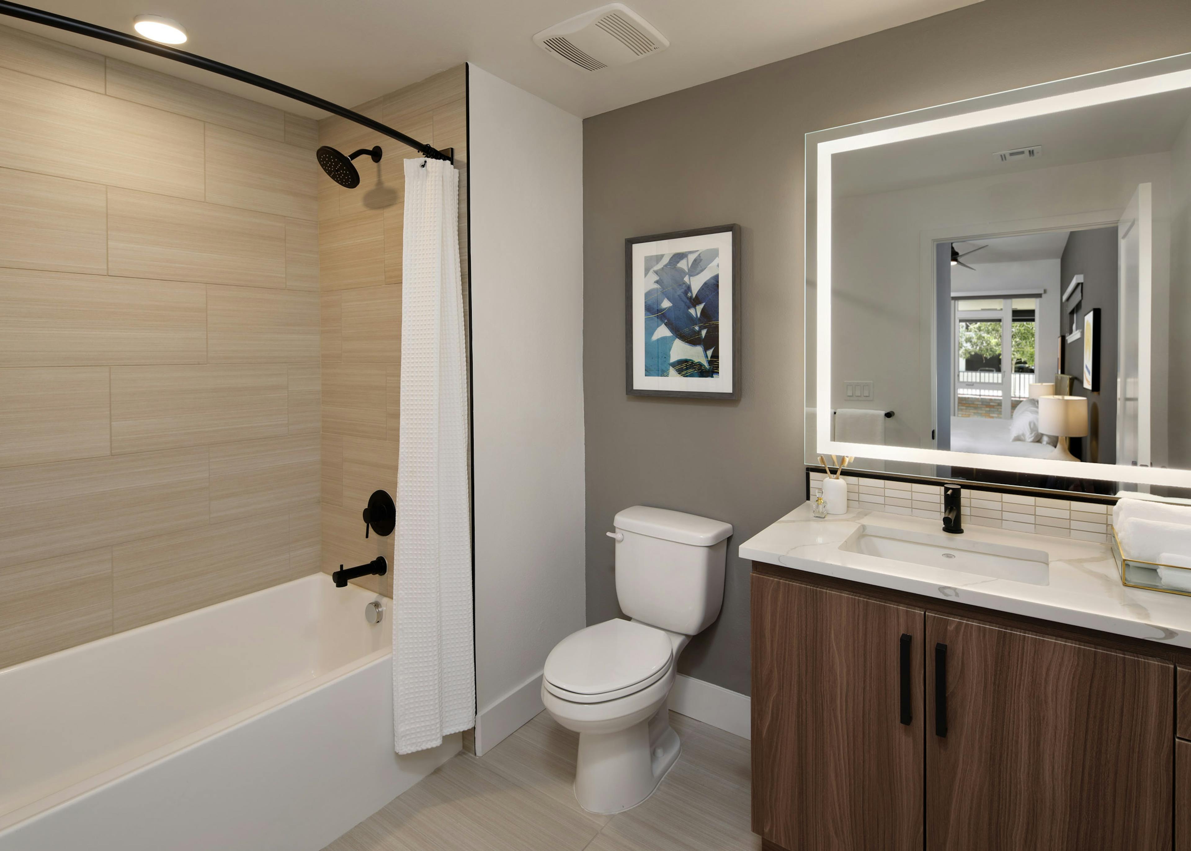 Bathroom at AMLI Old Pasadena apartments with tub and dark cabinetry and quartz countertop and lighted framed mirror