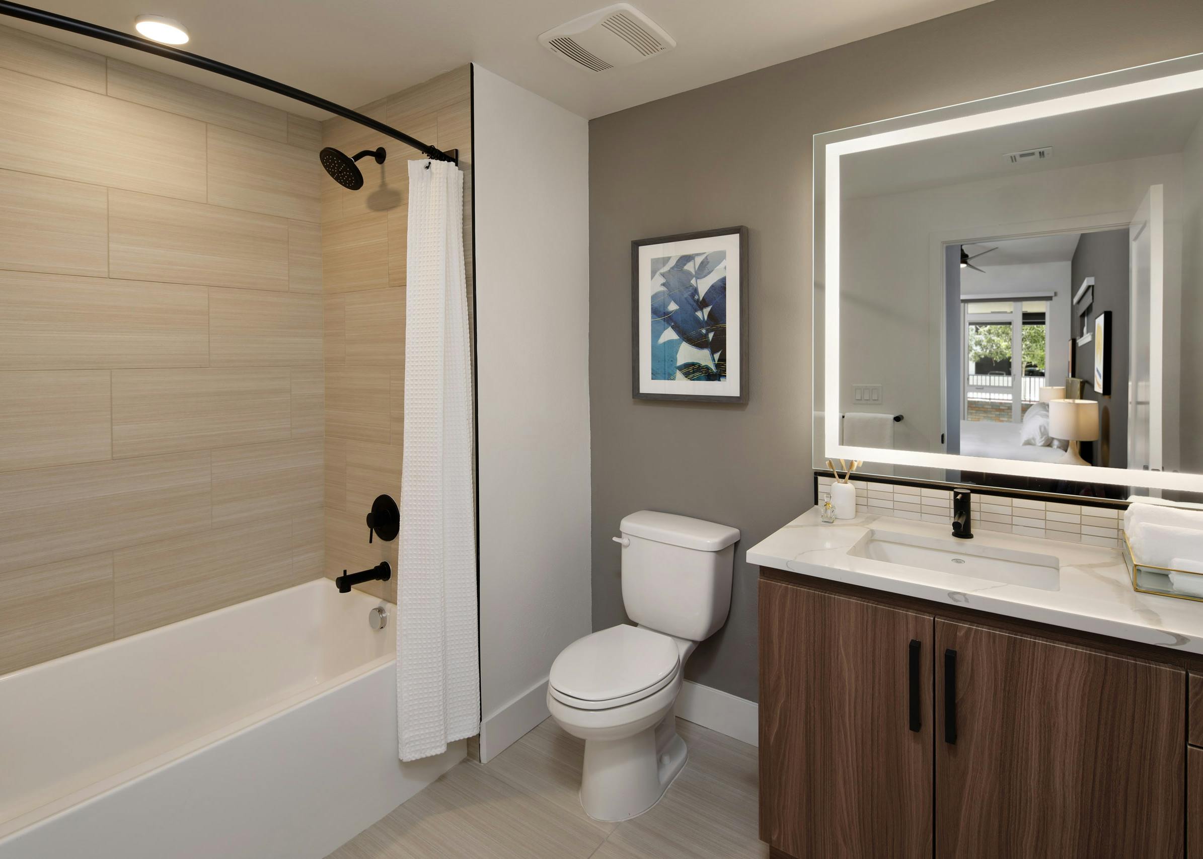 Bathroom at AMLI Old Pasadena apartments with tub and dark cabinetry and quartz countertop and lighted framed mirror