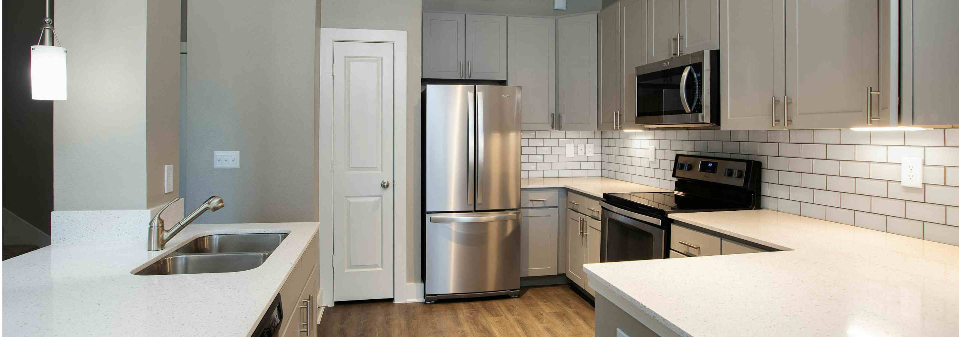 AMLI Eastside kitchen with grey cabinets and stainless steel appliances with dark hardwood flooring and a white pantry door