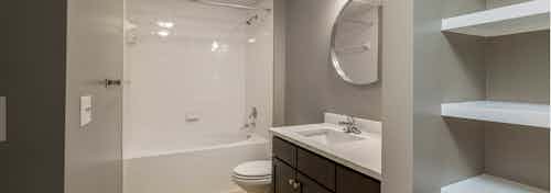 AMLI 5350 bathroom with grey walls and dark wood vanity sink with a round mirror and white shower tub with built in shelving