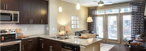 AMLI West Plano kitchen and living room with dark wood cabinets and floors with barstools and modern hanging light fixtures