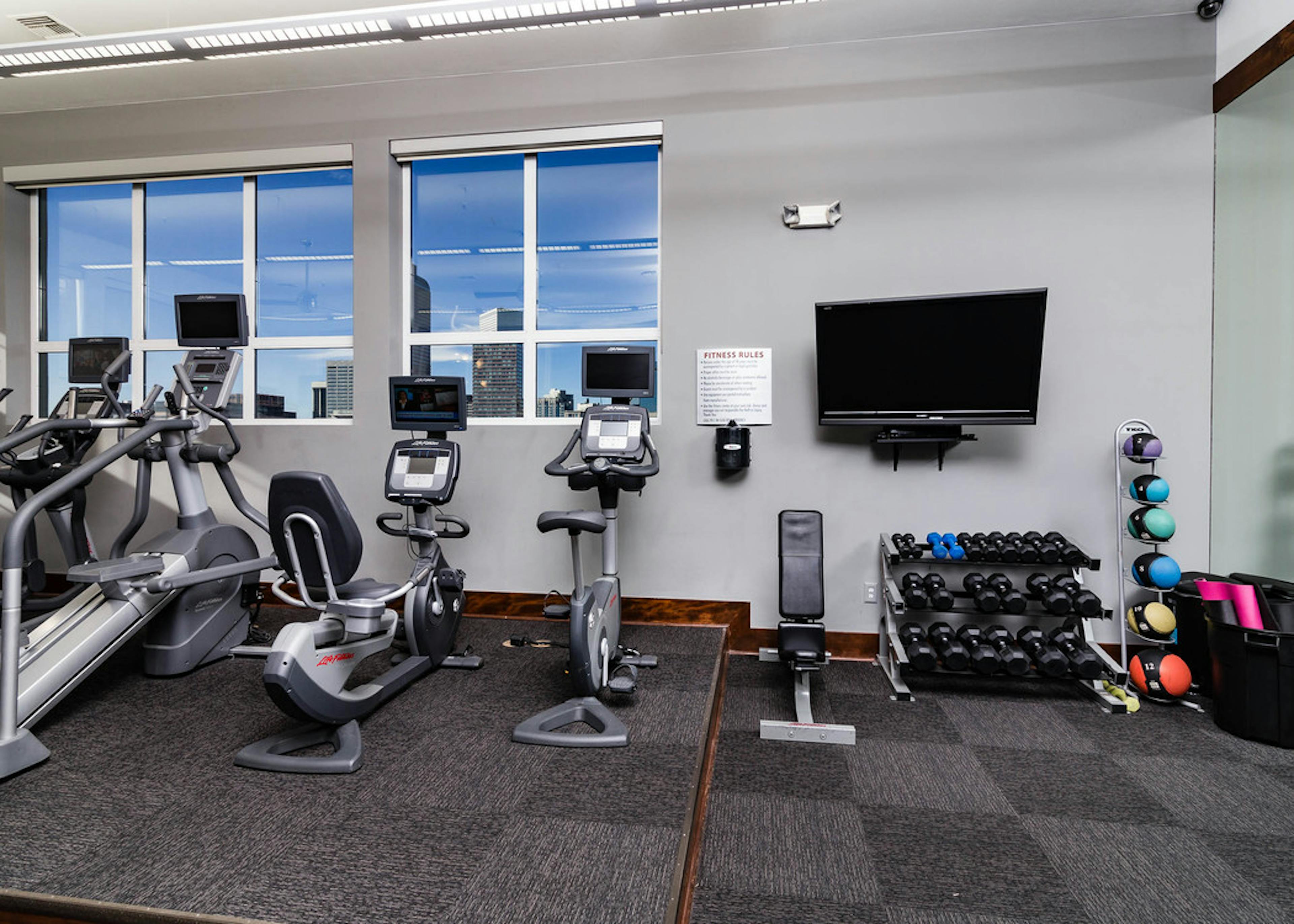 Interior view of a fitness center at AMLI Park Ave apartments with free weights and a television and various cardio machines