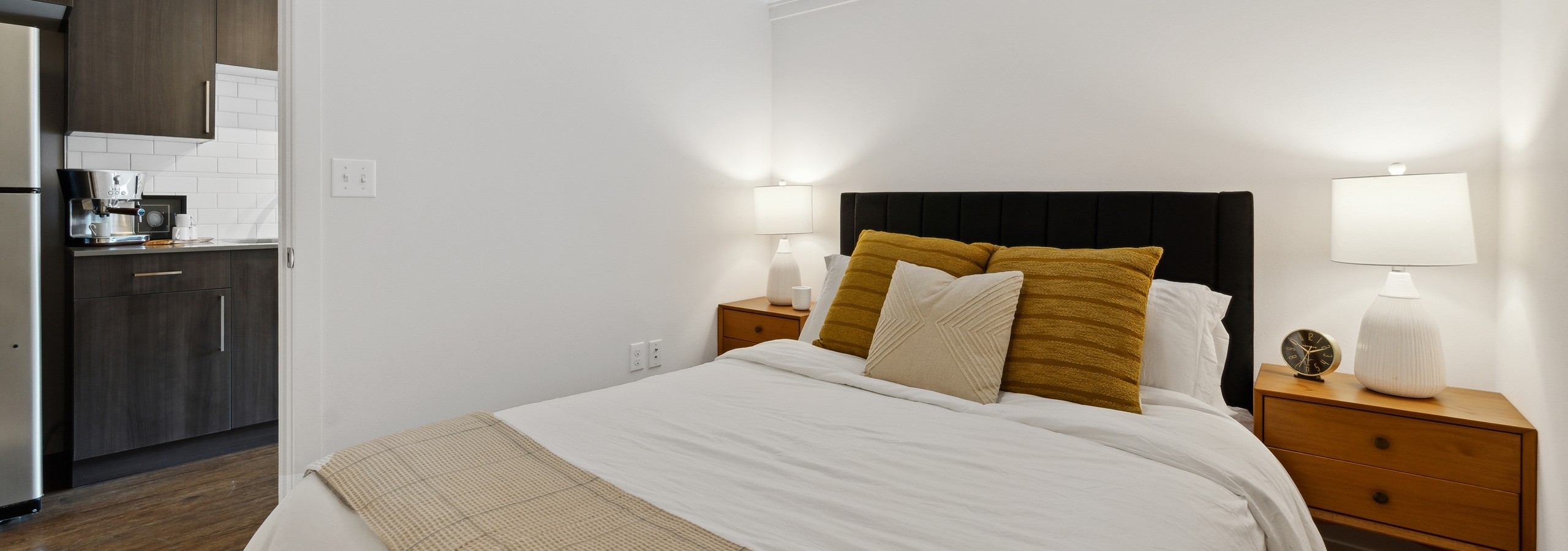 Interior view of a bedroom at AMLI South Lake Union with a bed and wooden side tables with lamps and a view into the kitchen