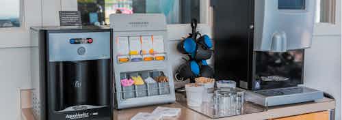 A java cafe at AMLI Arista apartments showcasing two coffee machines and mugs and sugar and creamers as well as many tea bags
