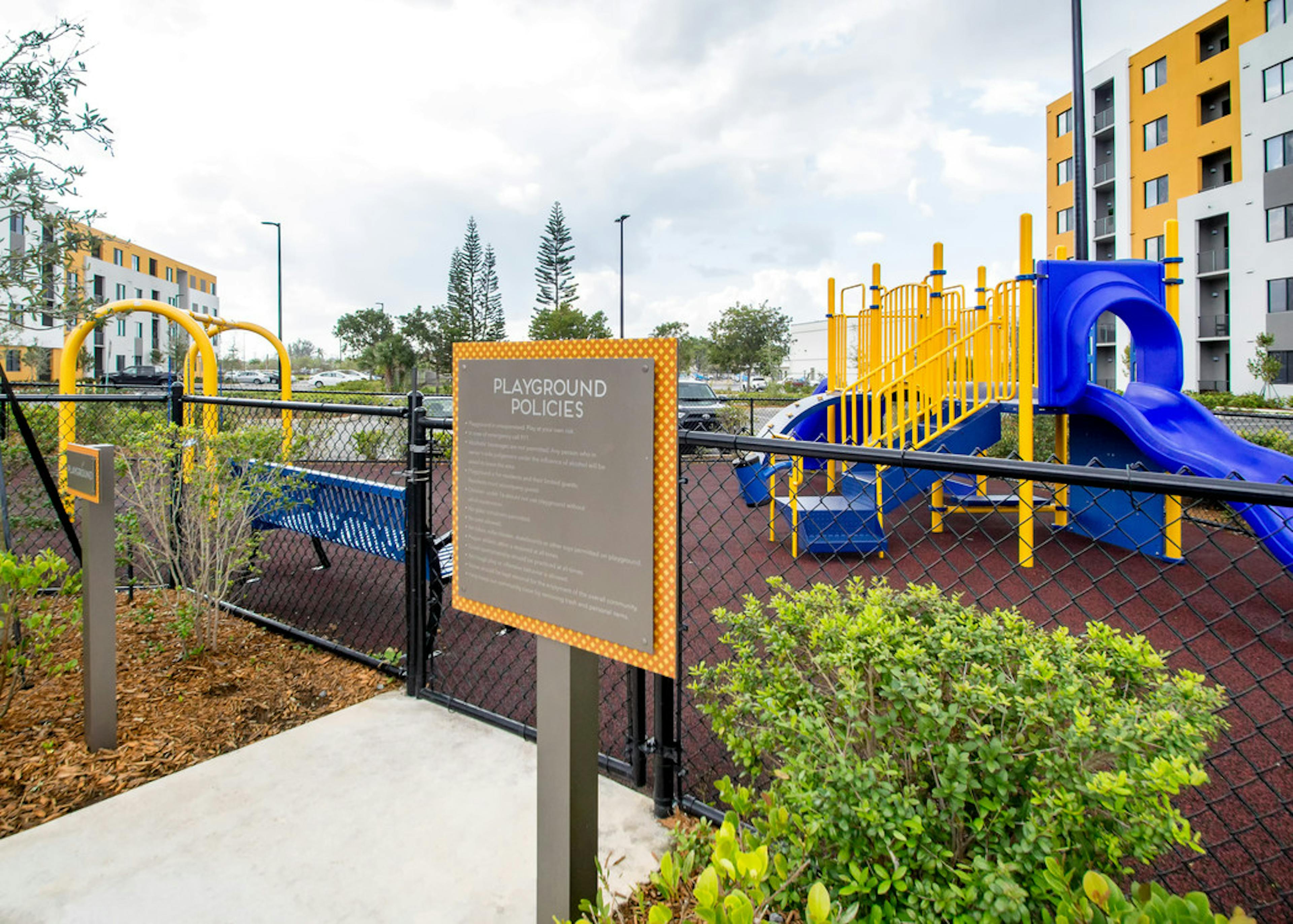 Outdoor bright yellow and blue children’s playground at AMLI 8800 featuring stairs for climbing, slide and swing set 