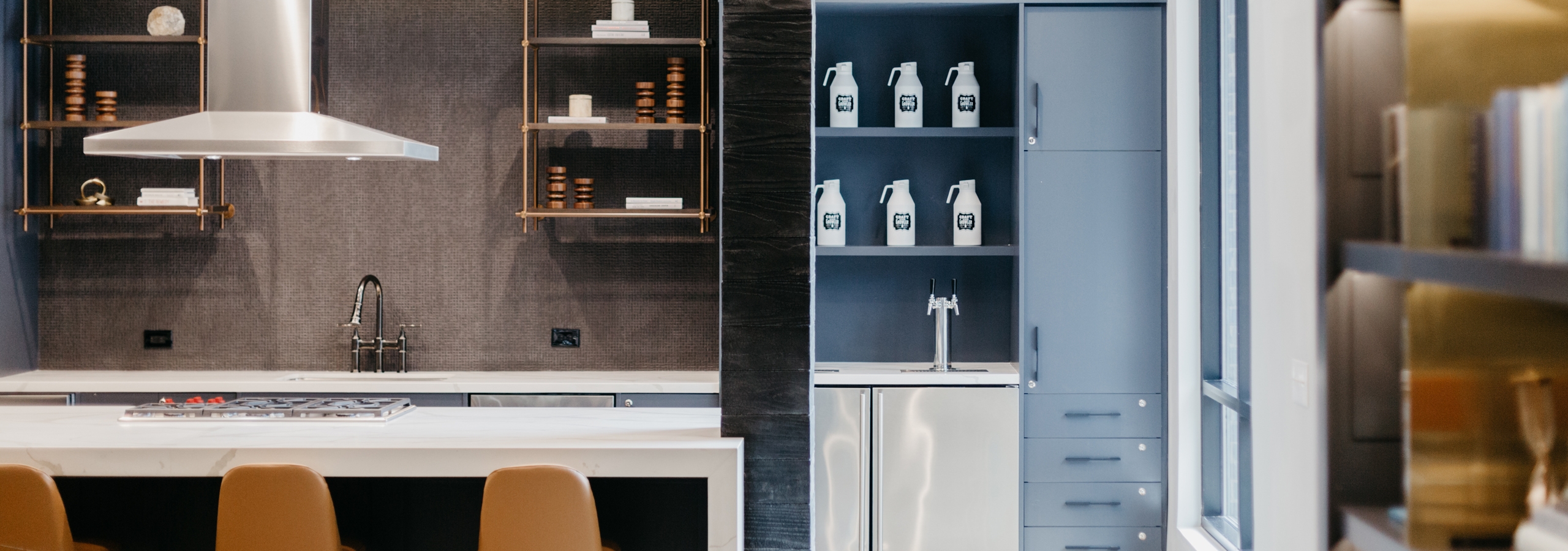 Kitchen area in the tap room at AMLI Addison with a long white counter and barstools with cabinets and shelves in background