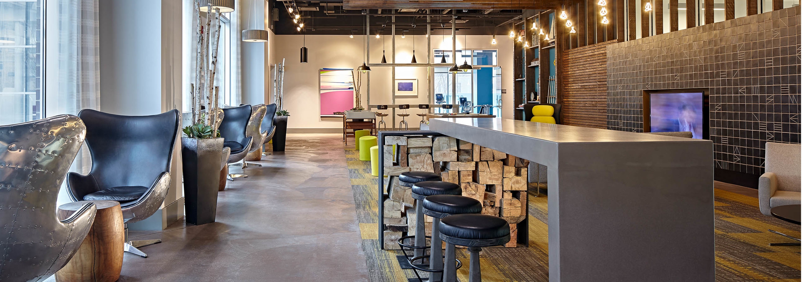 Lounge at AMLI Lofts which has bar stools and swivel chairs positioned by glass windows with hanging textured light fixtures