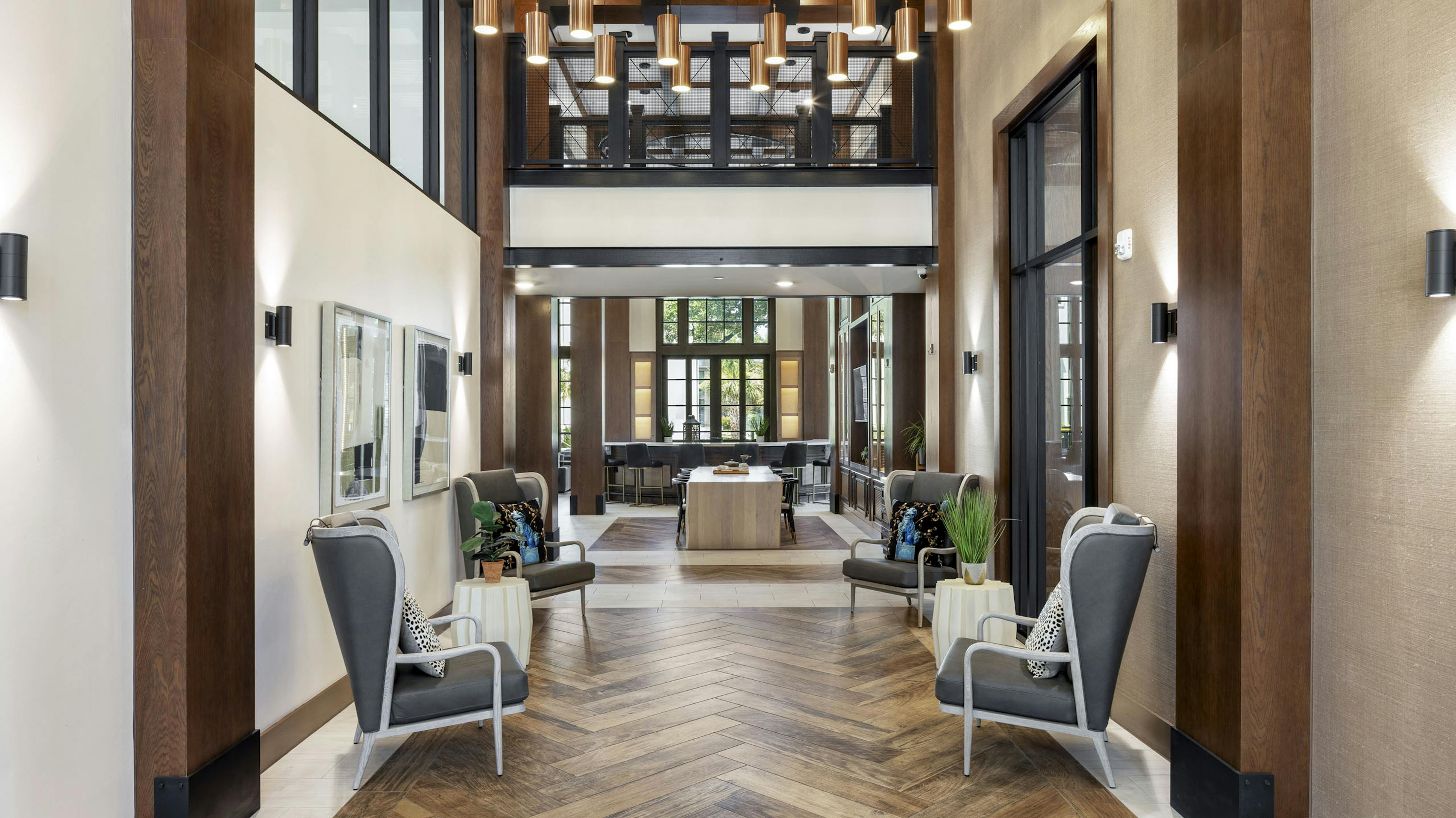 Entry to resident lounge at AMLI Lakeline with gray chairs and white side tables with wood flooring and two story ceiling 