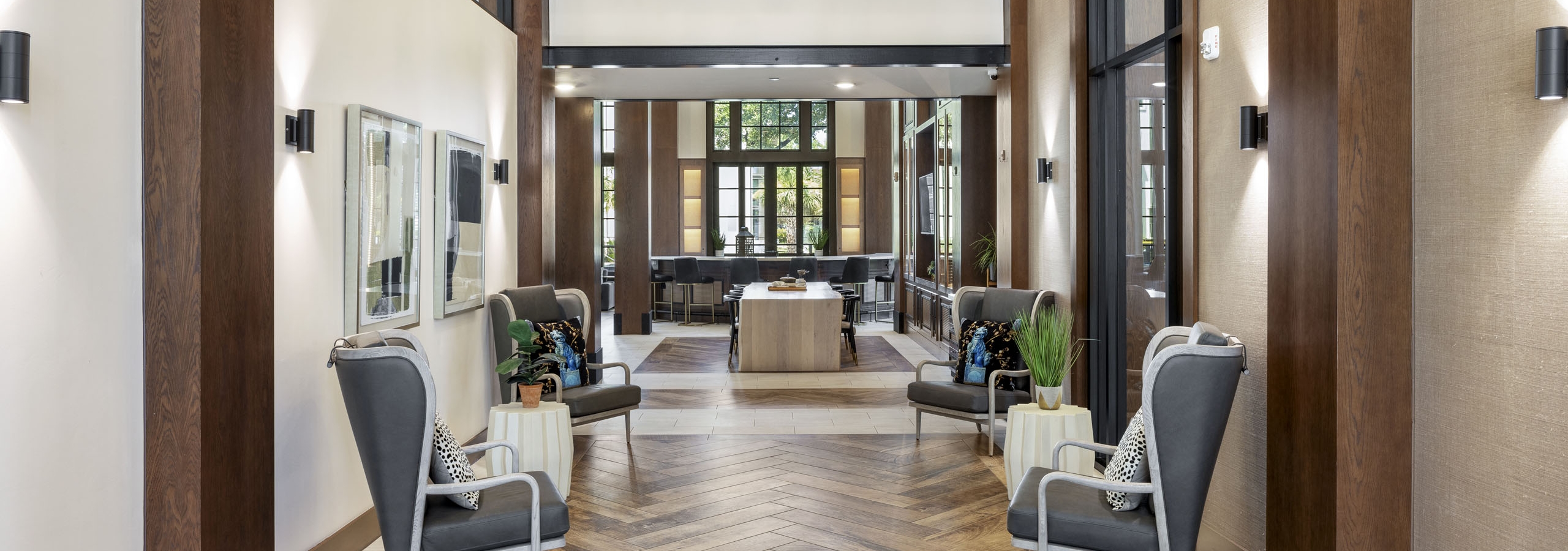 Entry to resident lounge at AMLI Lakeline with gray chairs and white side tables with wood flooring and two story ceiling