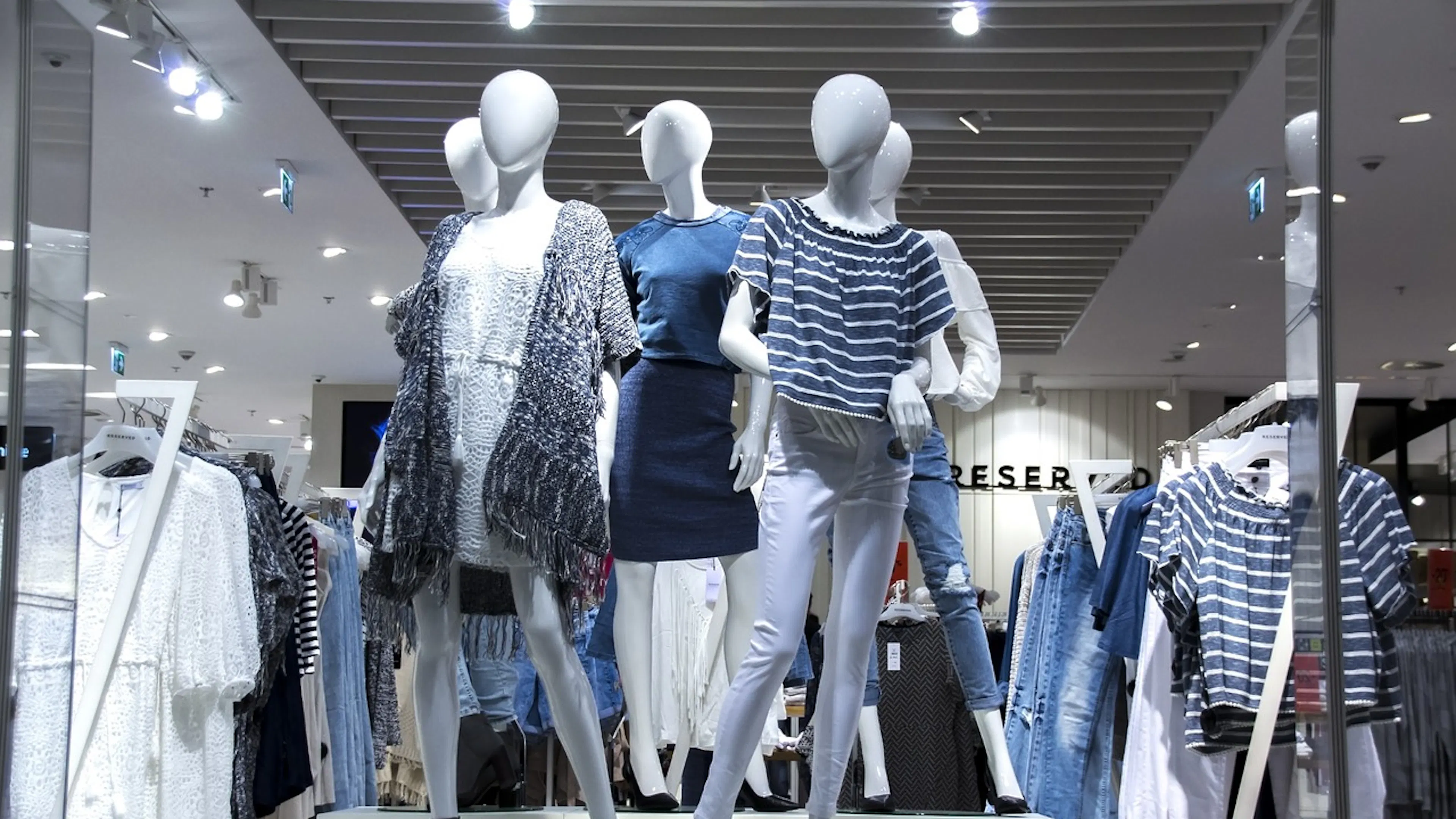 A group of five mannequins dressed in blue and white casual wear displayed in a glass windowfront