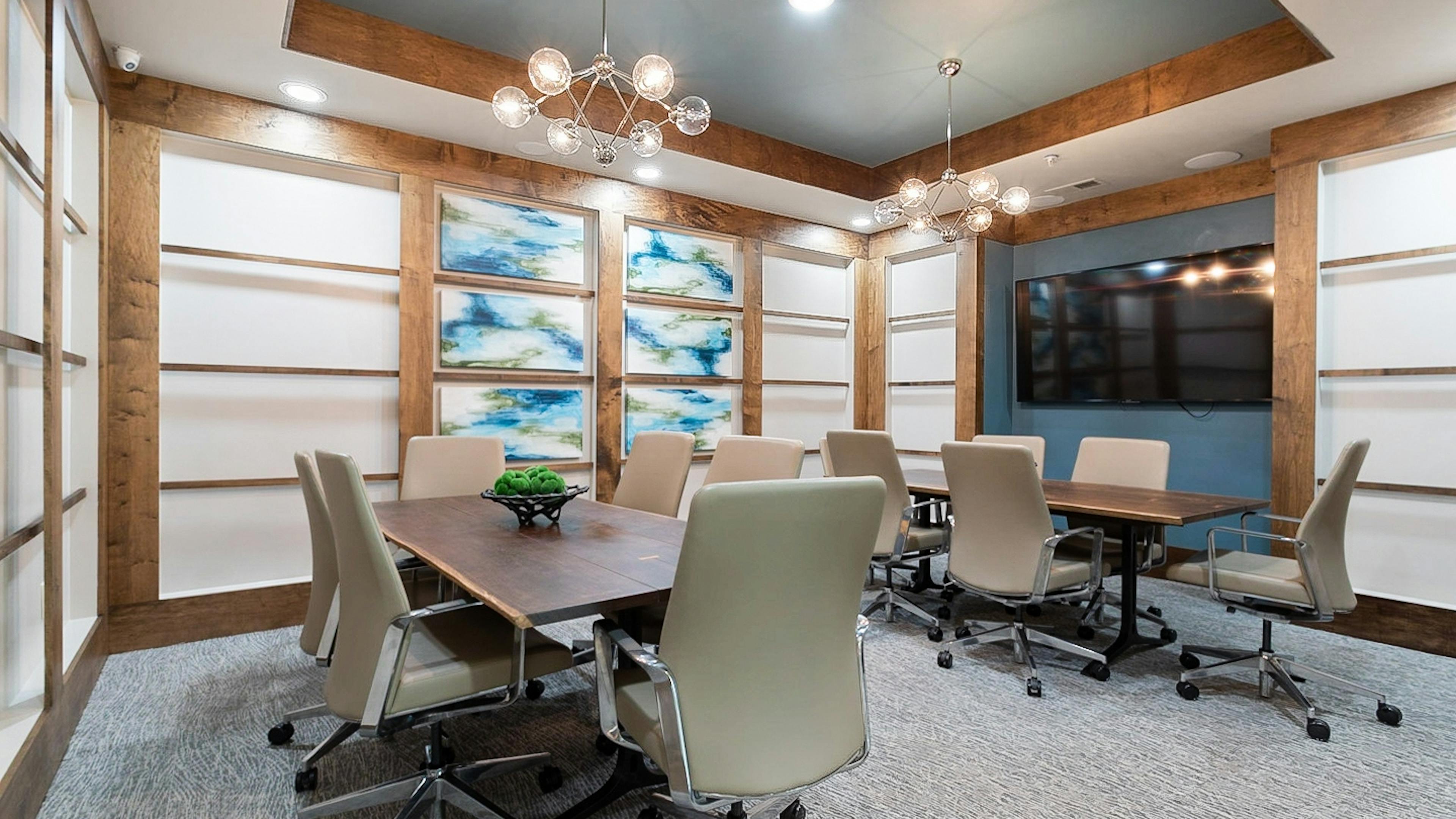 AMLI Old 4th Ward conference room with large TV and two large wood tables and six beige leather chairs at each