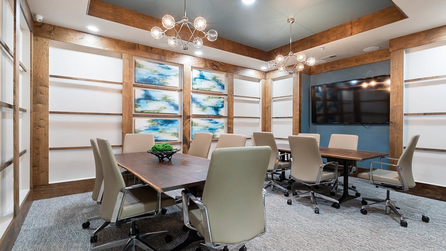 AMLI Old 4th Ward conference room with large TV and two large wood tables and six beige leather chairs at each