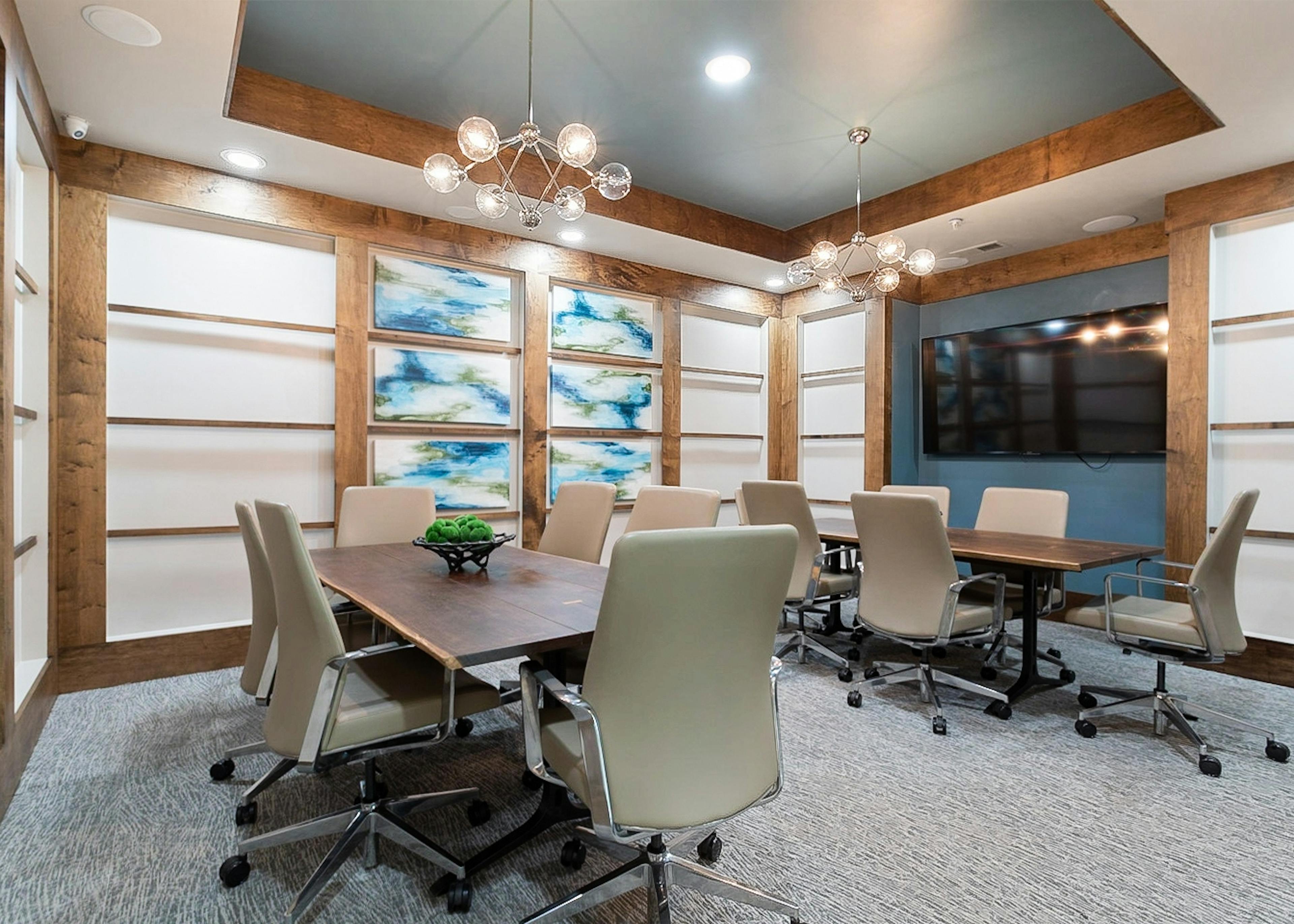 AMLI Old 4th Ward conference room with large TV and two large wood tables and six beige leather chairs at each