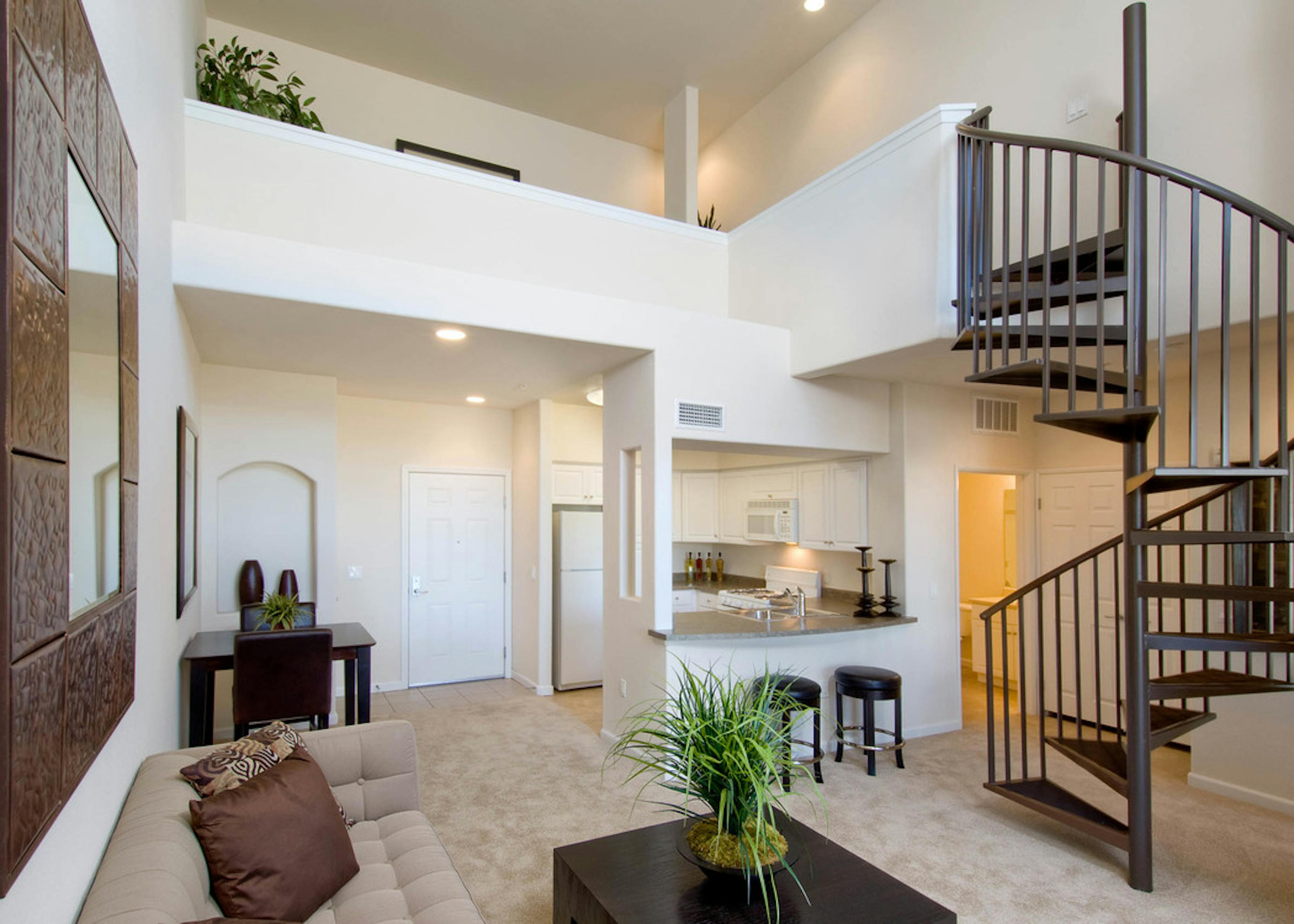 Interior of AMLI Warner Center apartment kitchen and living room with spiral staircase, carpet and peek into lit bathroom