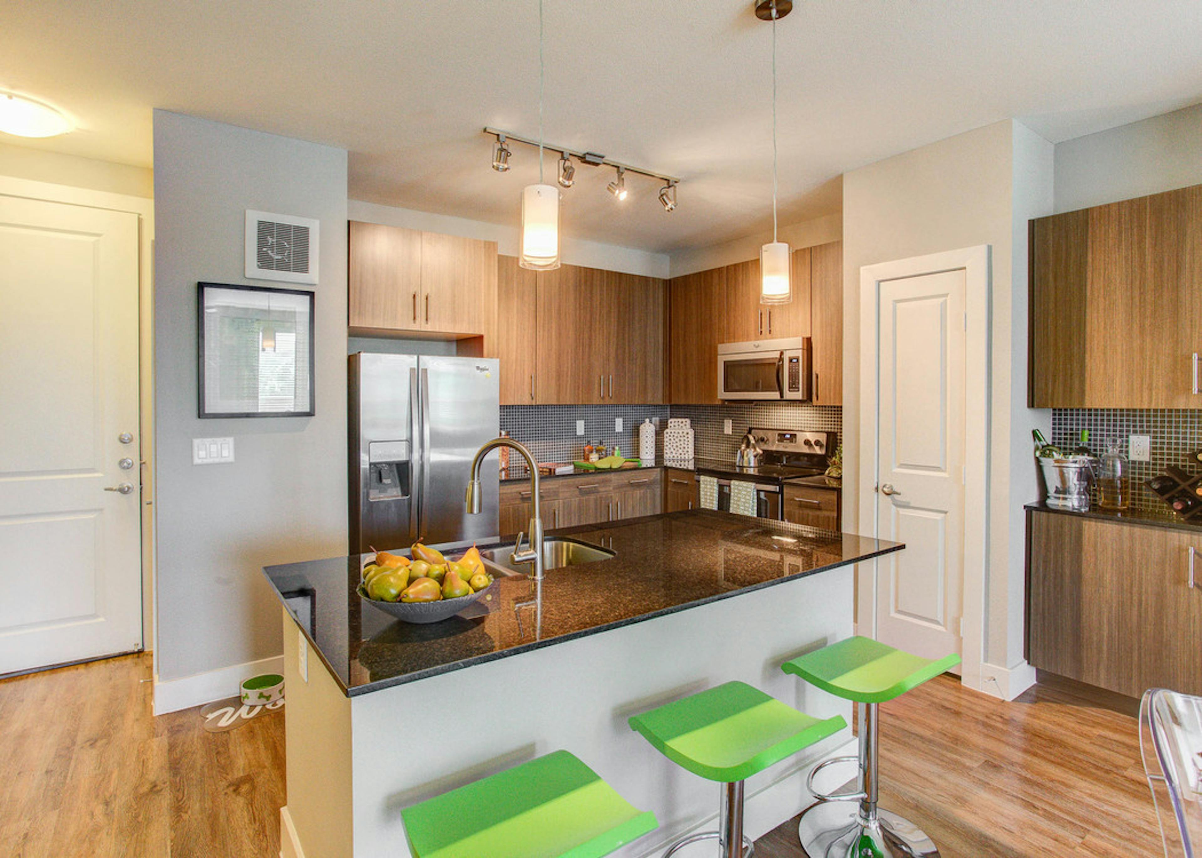 Interior view of a kitchen at AMLI Riverfront Park apartments with an island with stools and hard wood floors and cupboards 