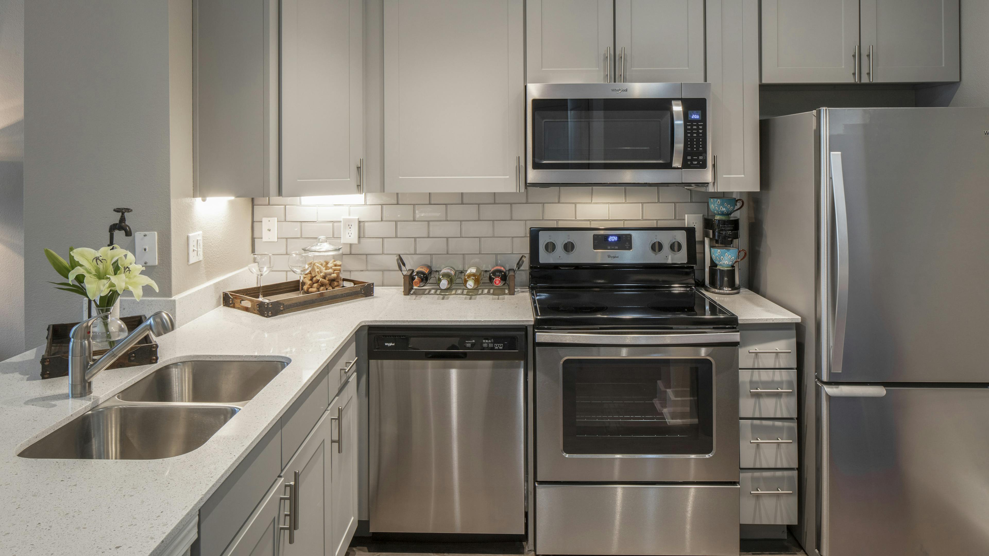 AMLI Eastside kitchen with stainless l appliances and quartz countertops with white cabinets and white tile backsplash