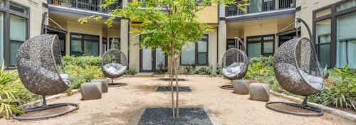 AMLI 5350 courtyard with circular grey wicker chairs and vibrant green bushes and trees with building facade in background