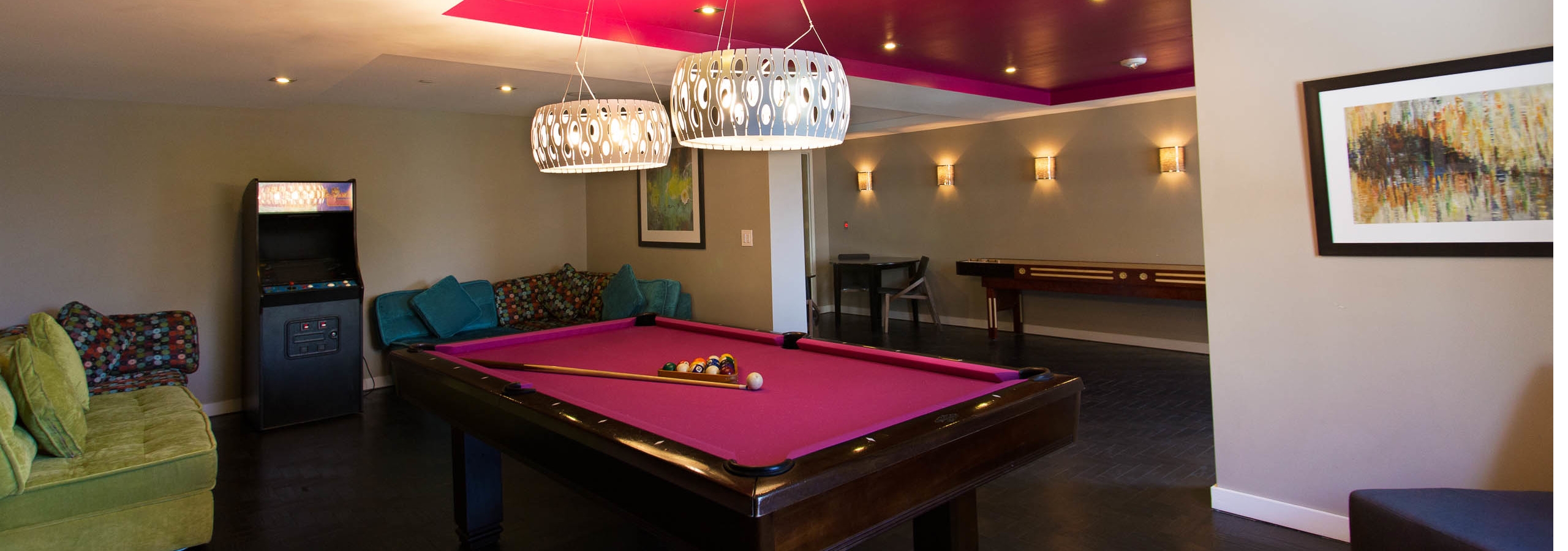 Interior game lounge at AMLI Dadeland with vibrant colored billiards table, arcade game and plush seating