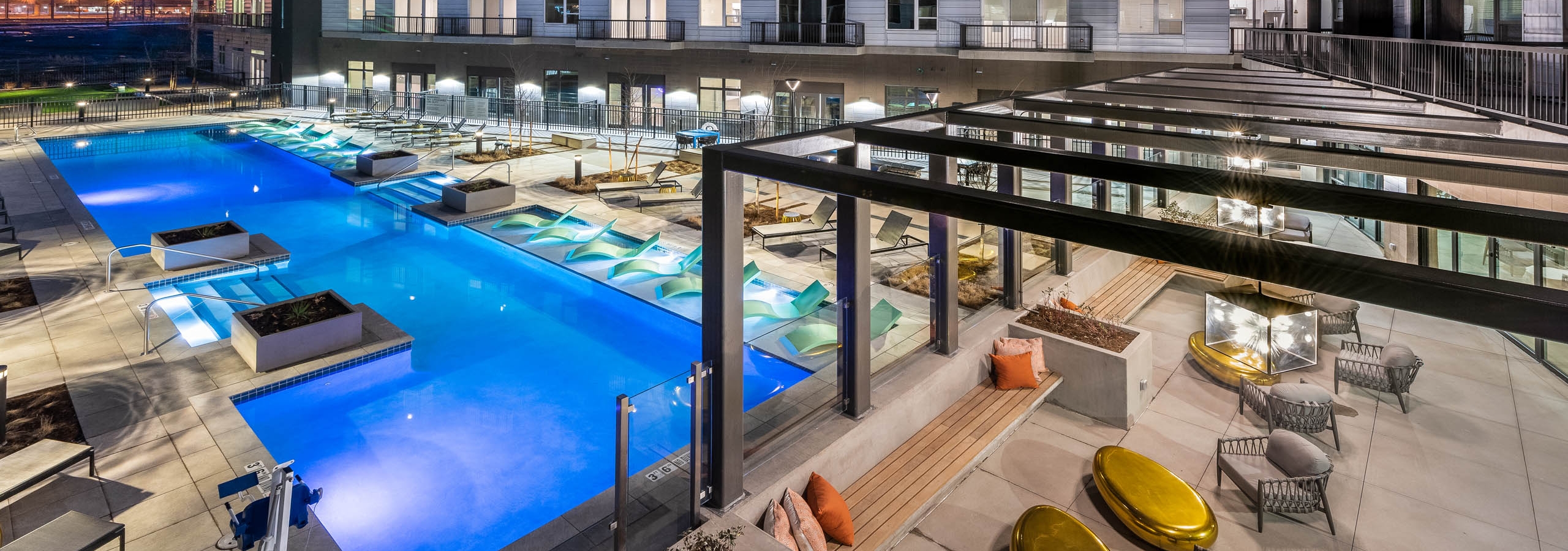 AMLI Art District swimming pool at night with several lounge chairs and planter boxes and view of the outdoor resident lounge