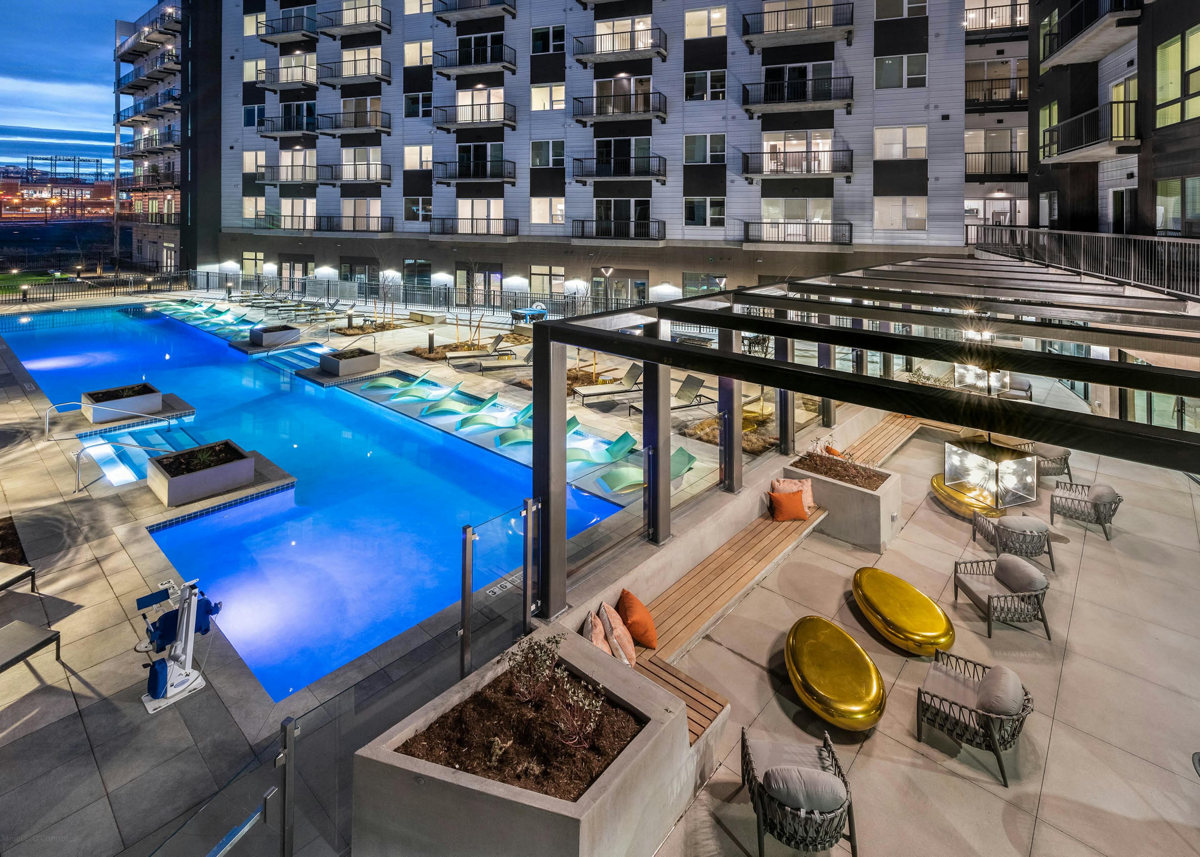 AMLI Art District swimming pool at night with several lounge chairs and planter boxes and view of the outdoor resident lounge