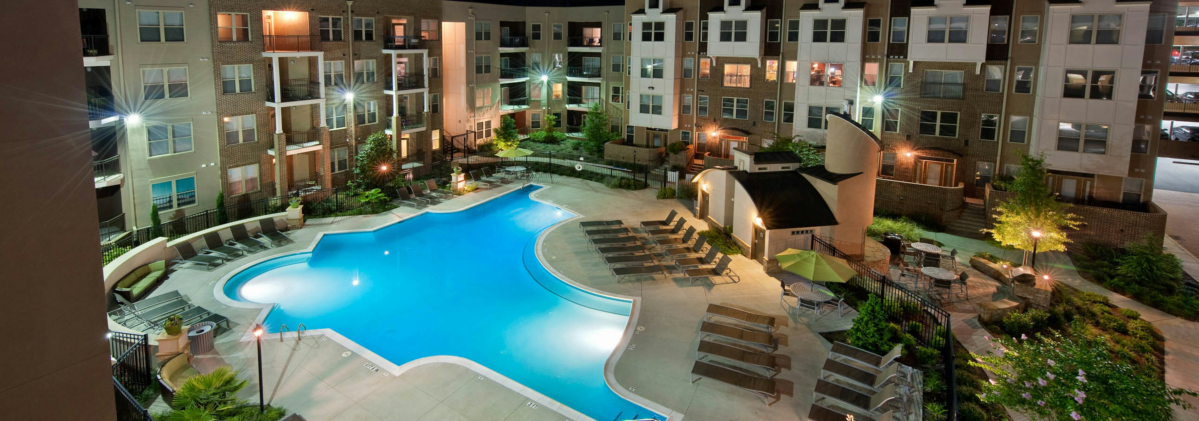 Ariel view of AMLI Lindbergh apartment community with a large well lit pool and surrounding lounge chairs at nighttime