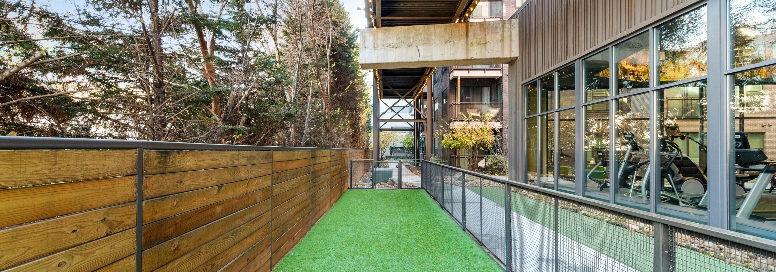 Daytime shot of long pet park run at AMLI Westside apartments with turf and wooden fence on one side facing fitness center