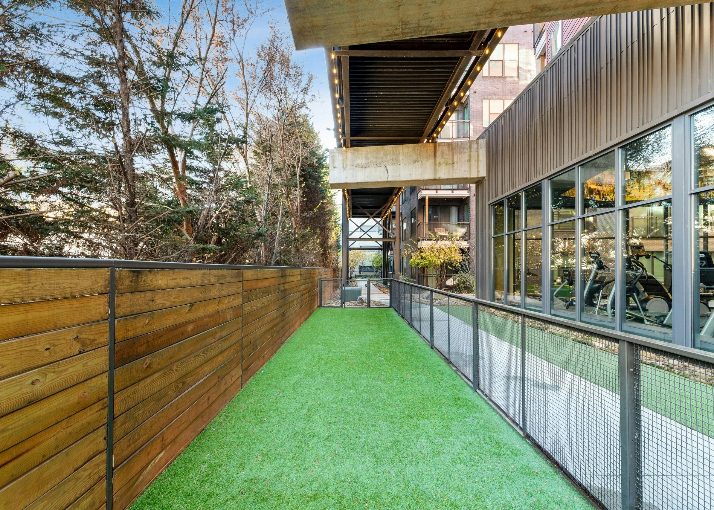 Daytime shot of long pet park run at AMLI Westside apartments with turf and wooden fence on one side facing fitness center