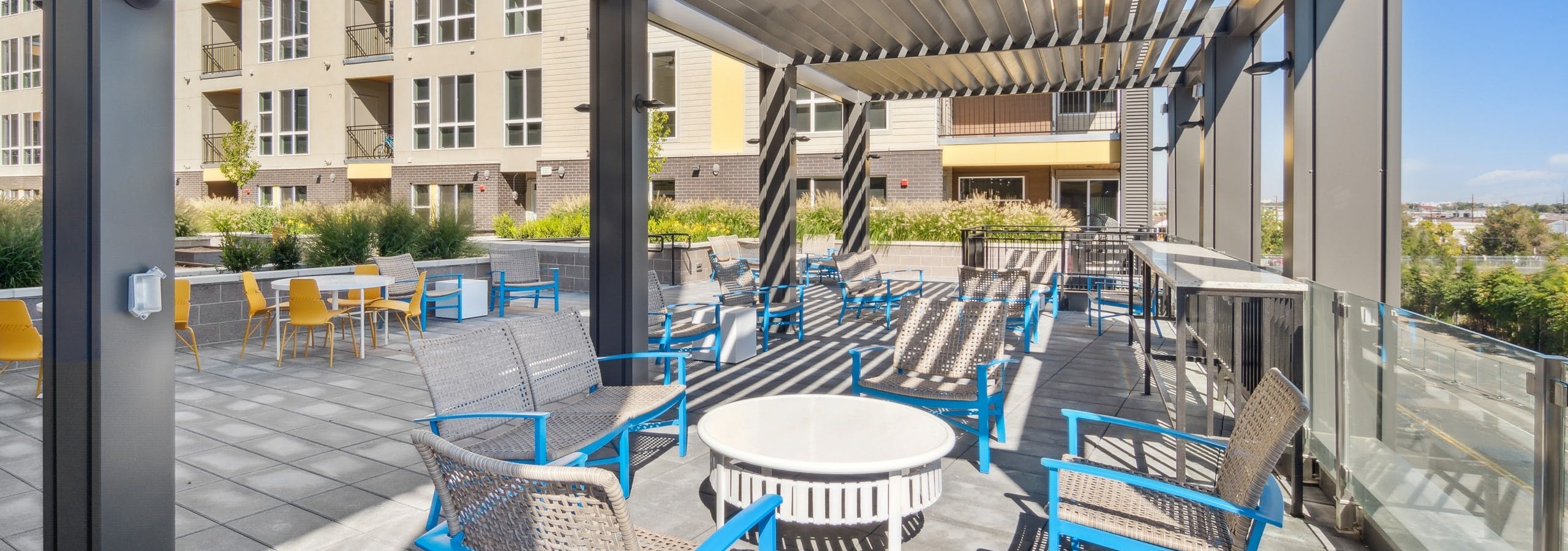 View of courtyard at AMLI RiNo with louvered cover and blue and yellow patio seating with view to the city
