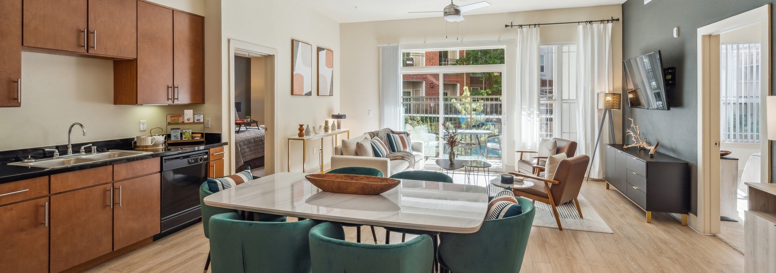 Kitchen and living room at AMLI Park Avenue with dining table and 6 teal chairs facing living room and view to patio