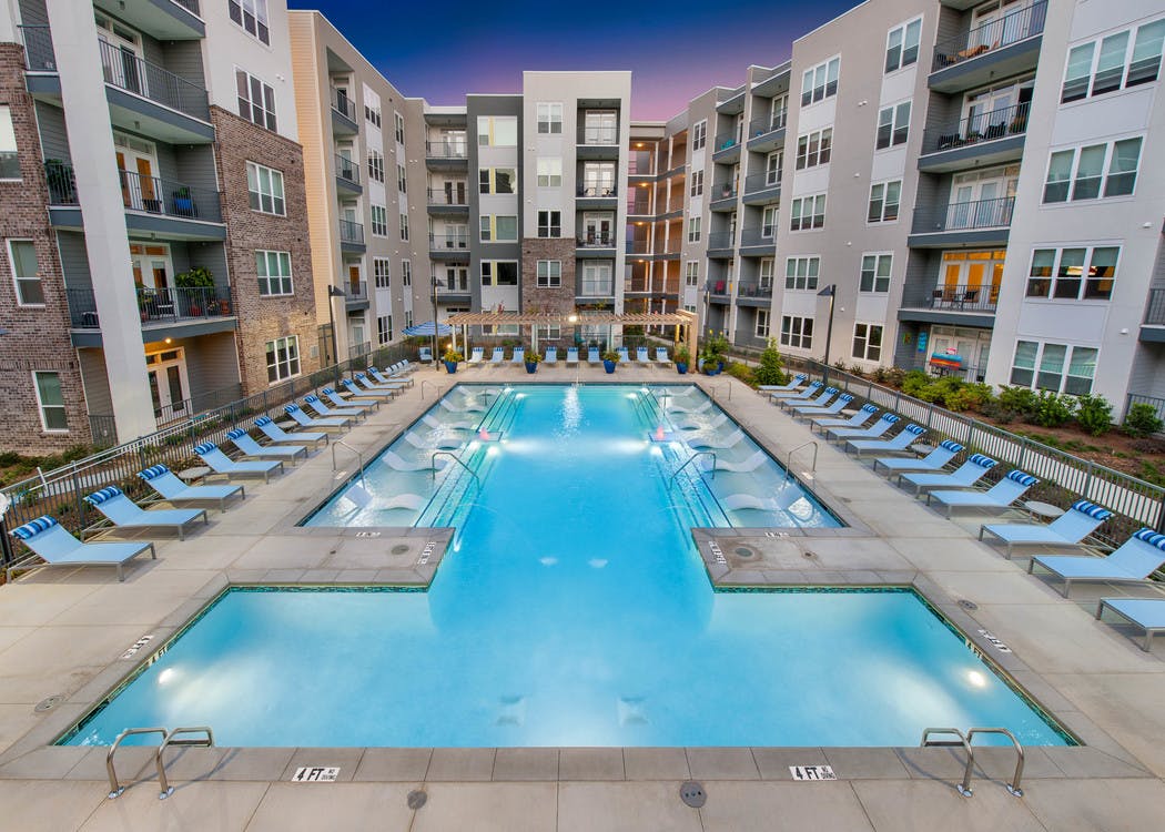 Exterior of AMLI Piedmont Heights pool at dusk featuring in water ledge loungers framed by lounge chairs and bright plants
