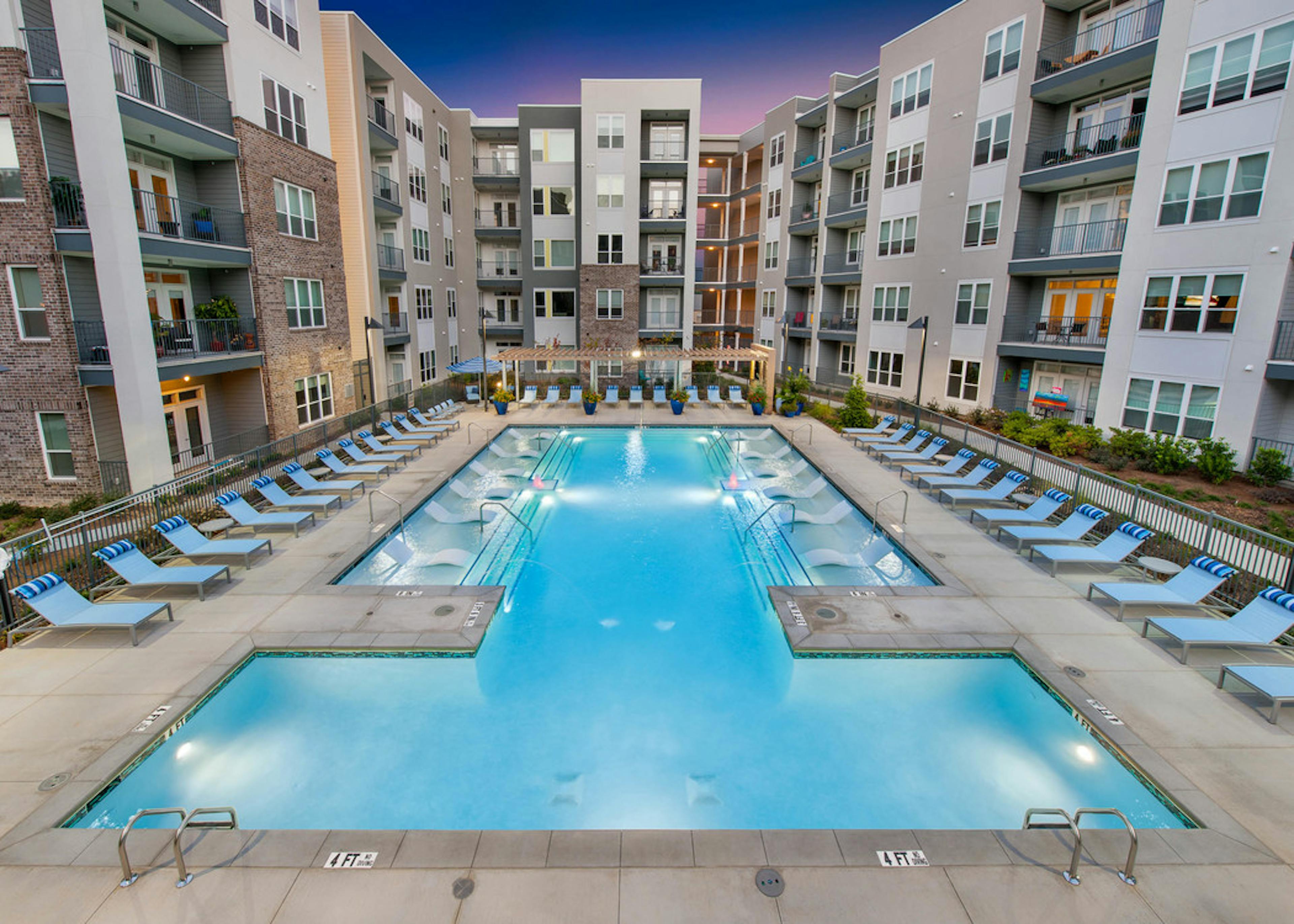 Exterior of AMLI Piedmont Heights pool at dusk featuring in water ledge loungers framed by lounge chairs and bright plants