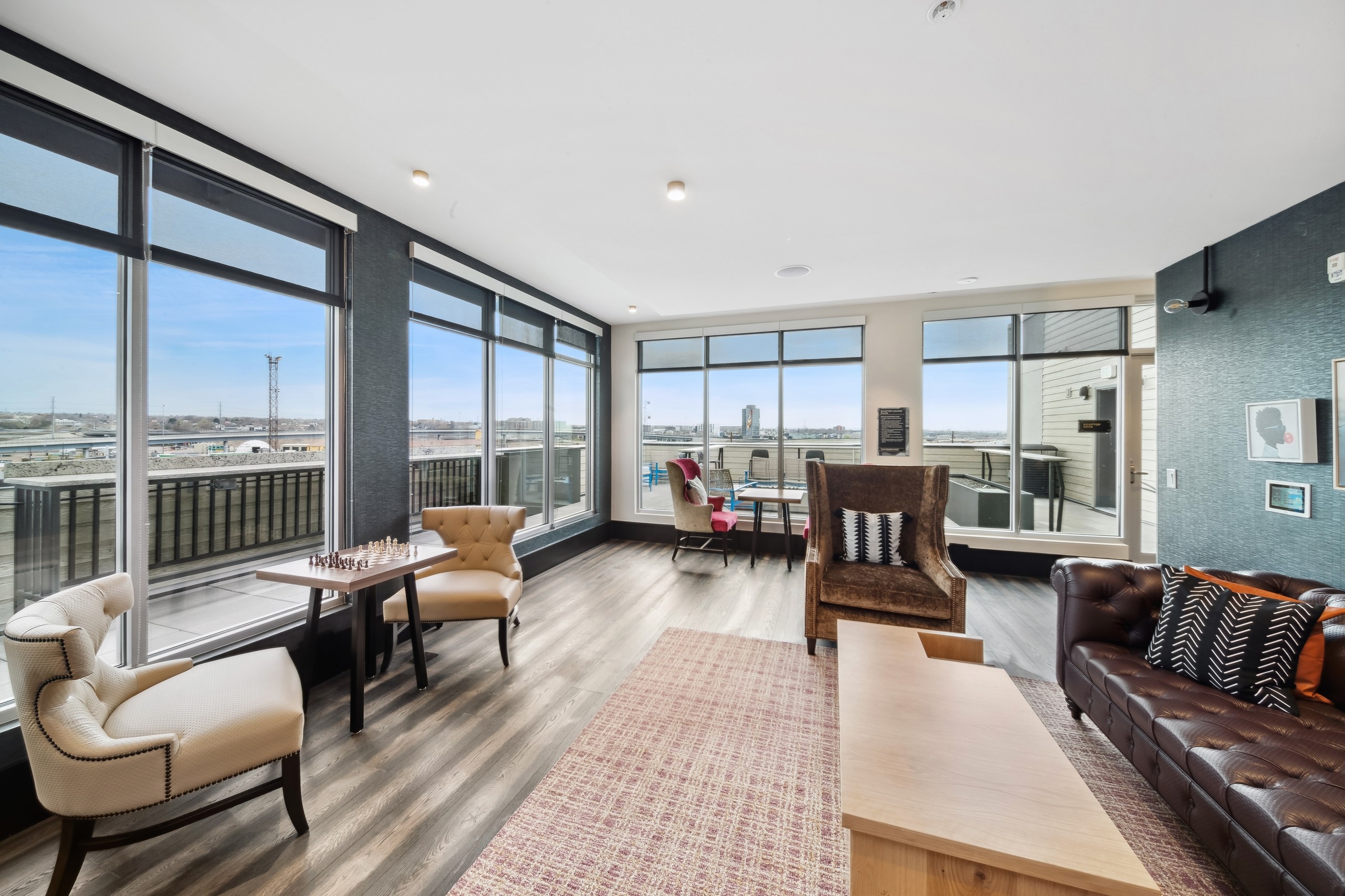 Skydeck lounge at AMLI RiNo with a brown leather couch and coffee table and chess table with 2 chairs and 2 walls of windows