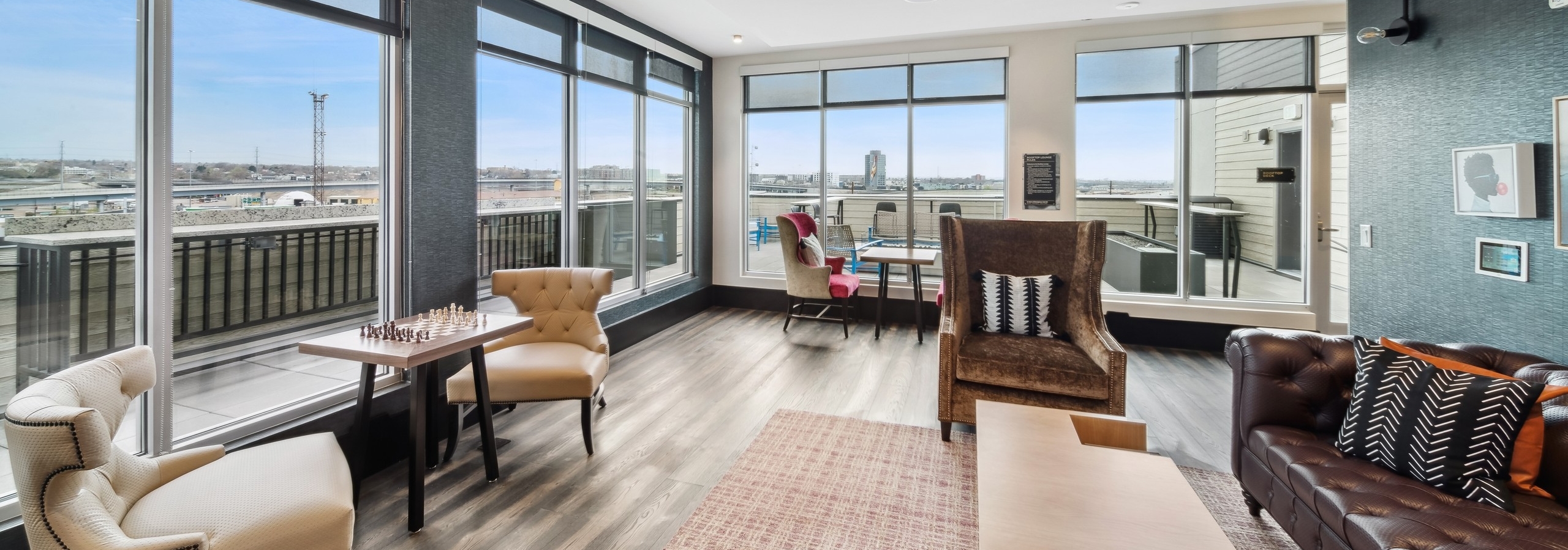 Skydeck lounge at AMLI RiNo with a brown leather couch and coffee table and chess table with 2 chairs and 2 walls of windows