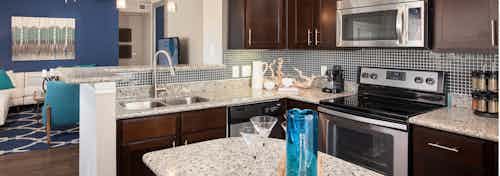 AMLI Memorial Heights apartment kitchen with dark wood cabinets and tile backsplash and granite island and countertops