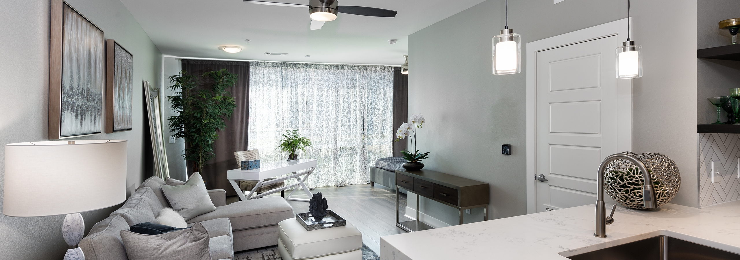 View of AMLI South Shore living room from kitchen showing dark floors and modern light fixtures with floor to ceiling windows